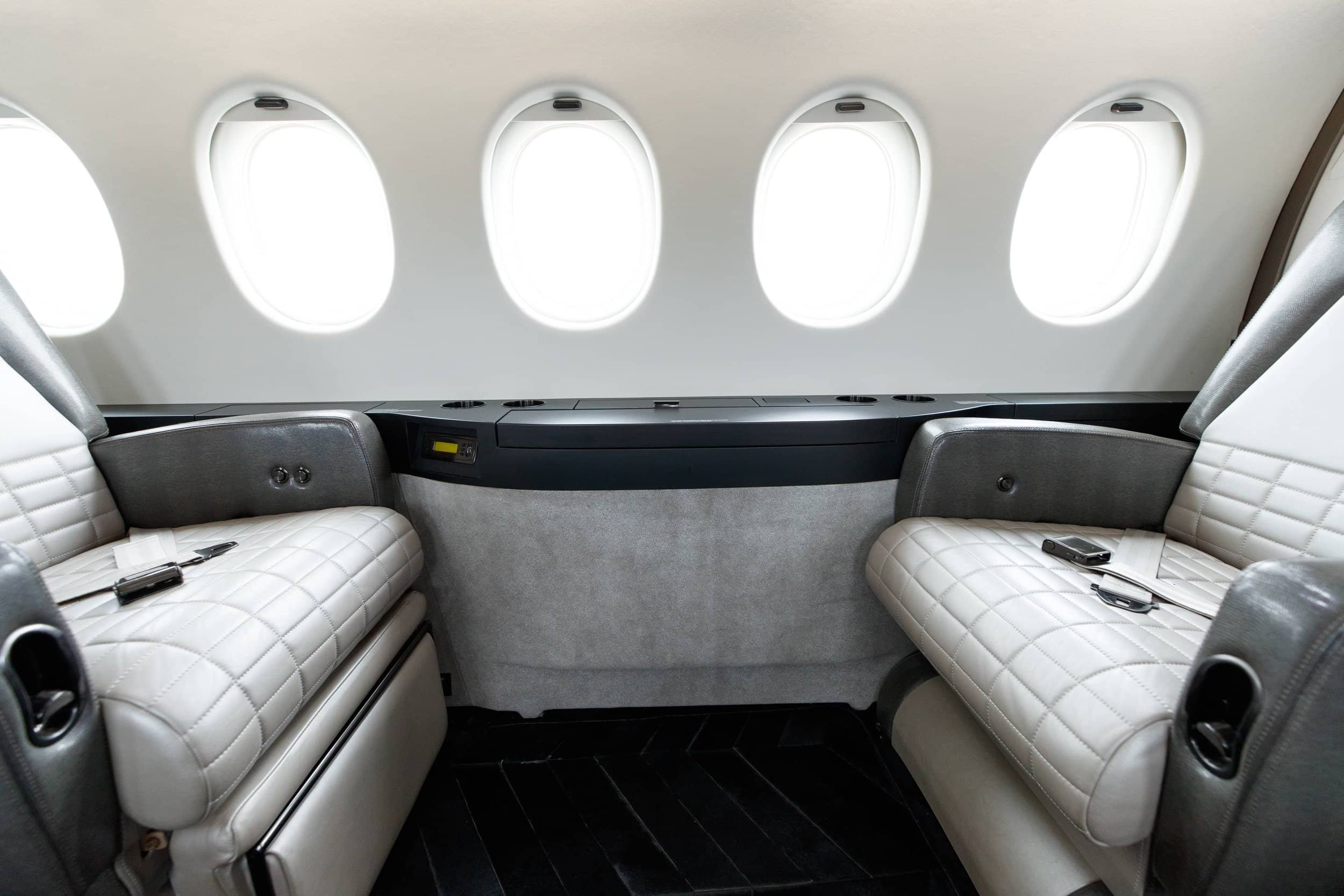 Interior of an airplane with two cream-colored leather seats, armrests, and window views.