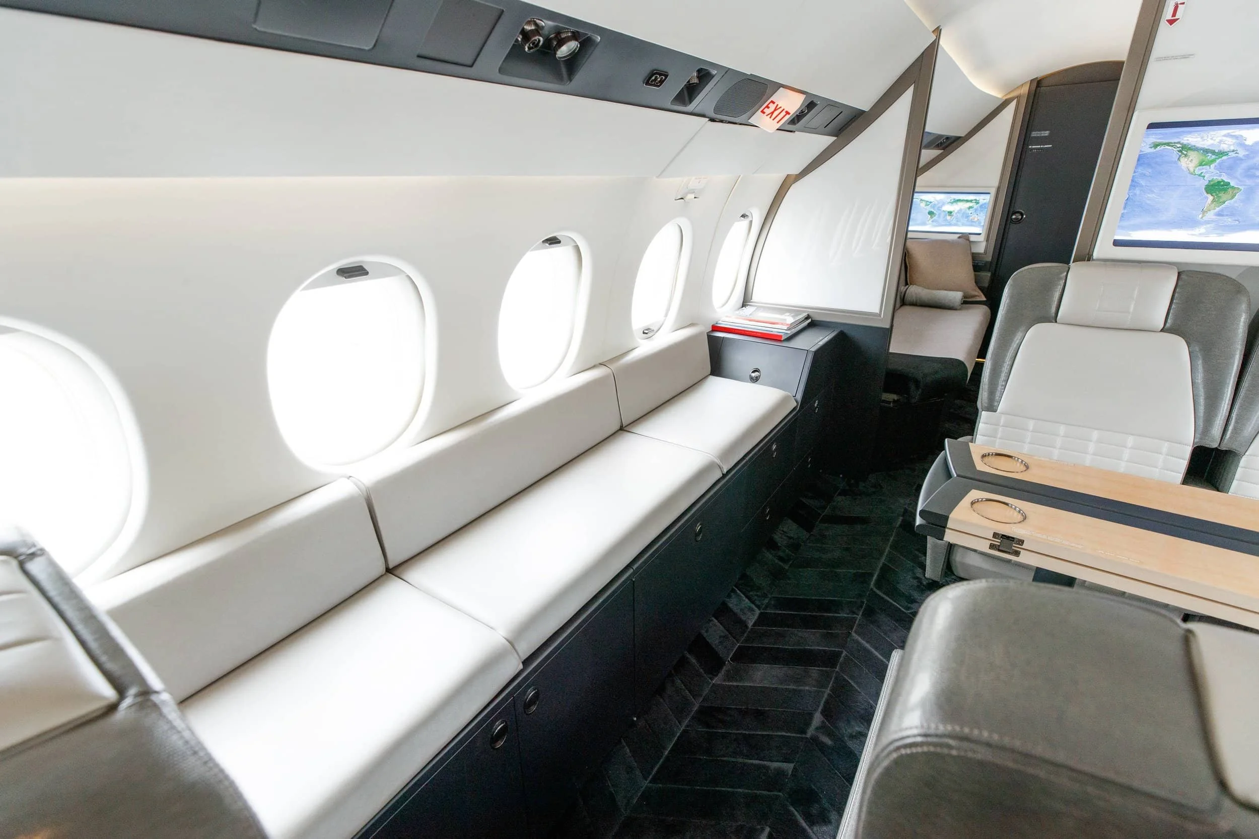 Interior of an airplane with beige seats, small tables, windows, and a world map on a display screen.