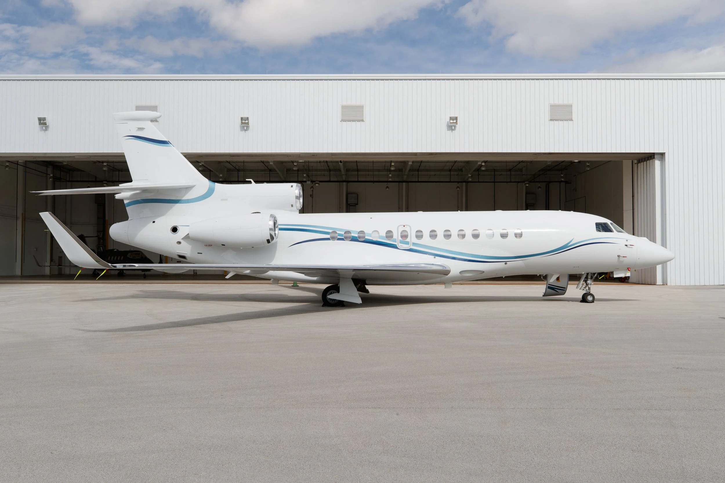 White private jet with blue accents parked outside hangar on tarmac.