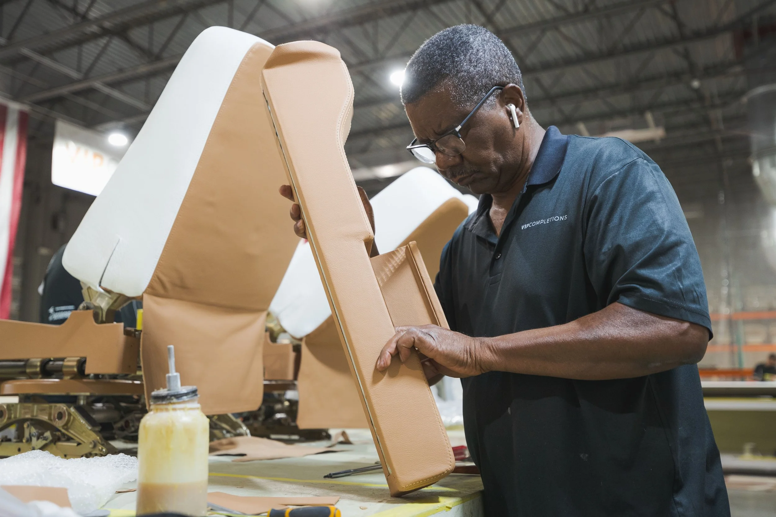 A worker inspecting a tan car seat in a manufacturing facility.