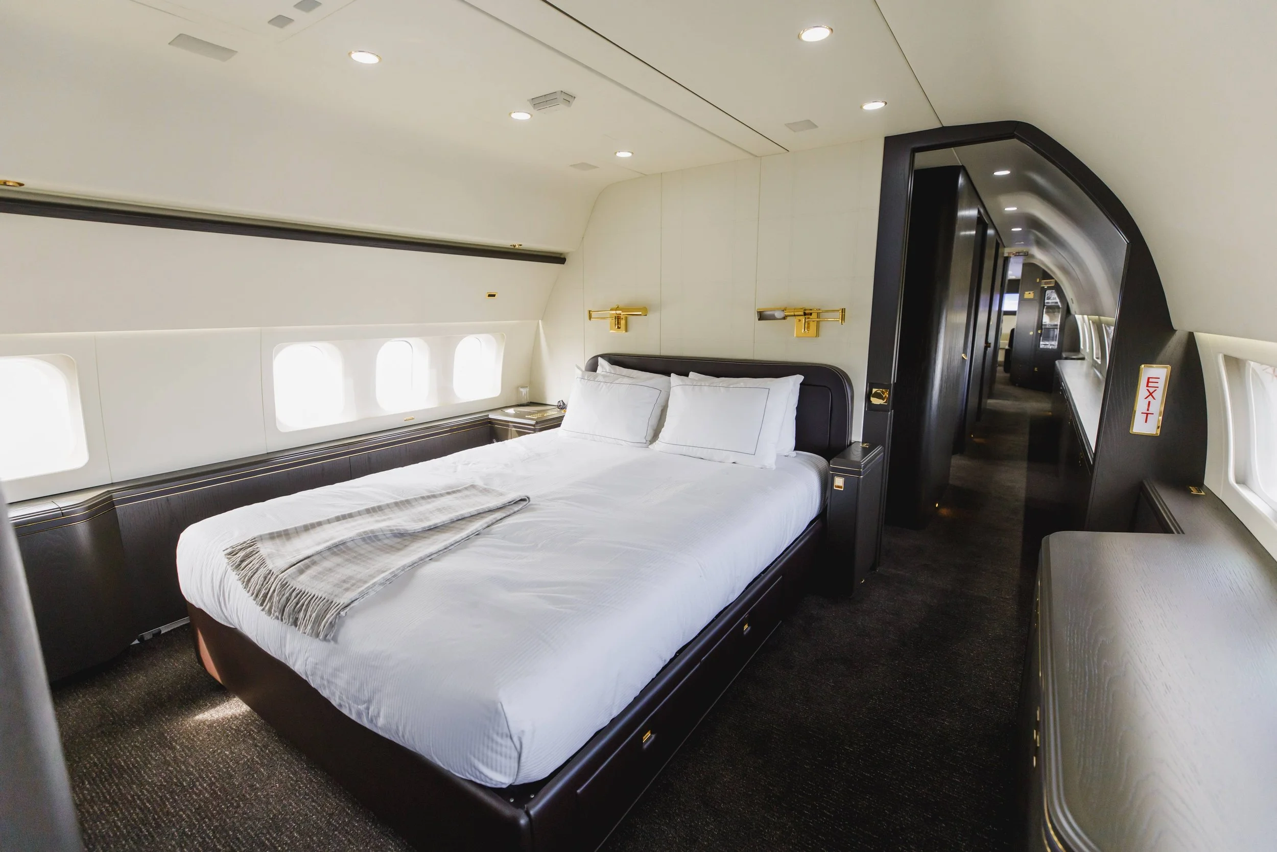 Luxury airplane hotel room with a large bed, black and gold accents, and windows along the wall.