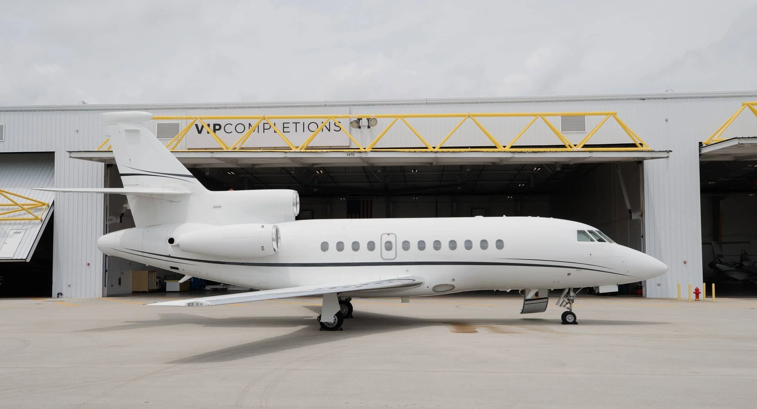 A white private jet parked outside a hangar at an airport, with a sign that reads VIP COMPLETIONS on the building.
