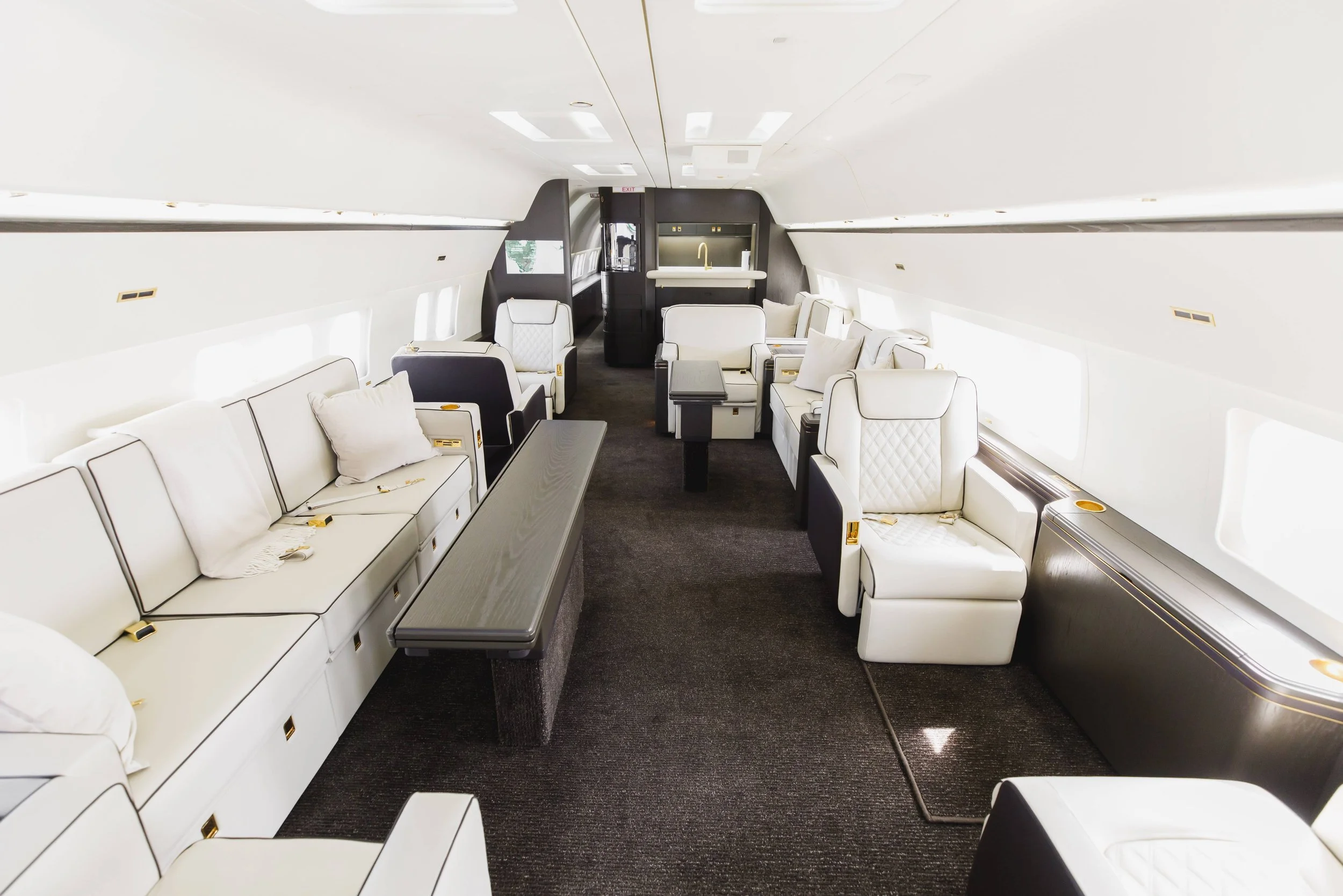 Luxury private jet interior with white leather seats, large windows, and dark wood accents.