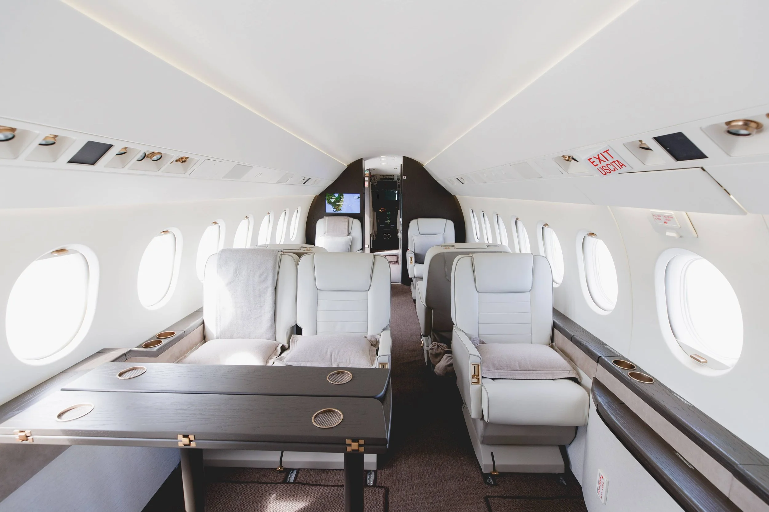 Empty airplane cabin with white leather seats, large windows, and overhead storage, viewed from the front toward the back.