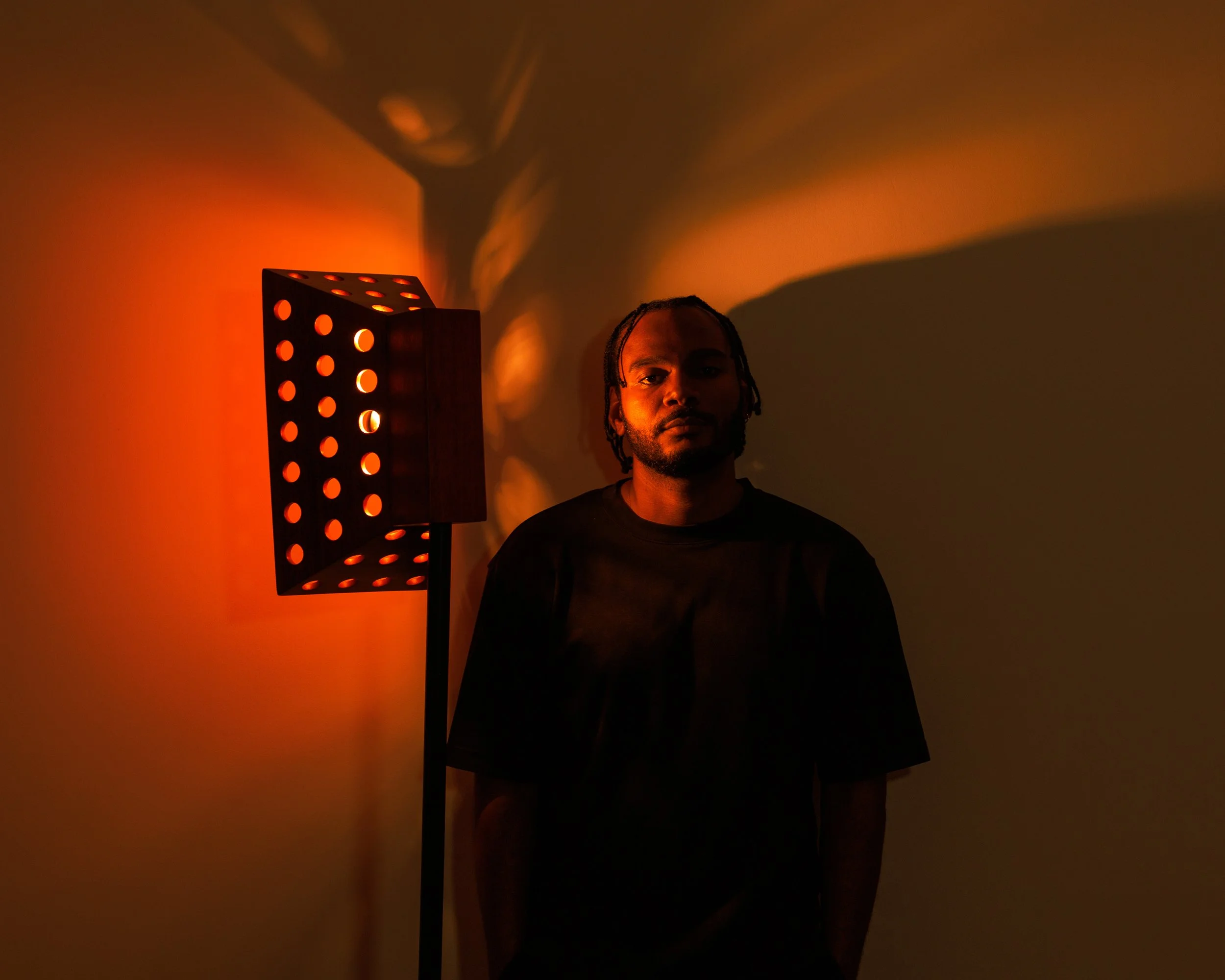 Un homme debout à côté d'une lampe avec un éclairage orange et des ombres projetées sur le mur derrière lui.
