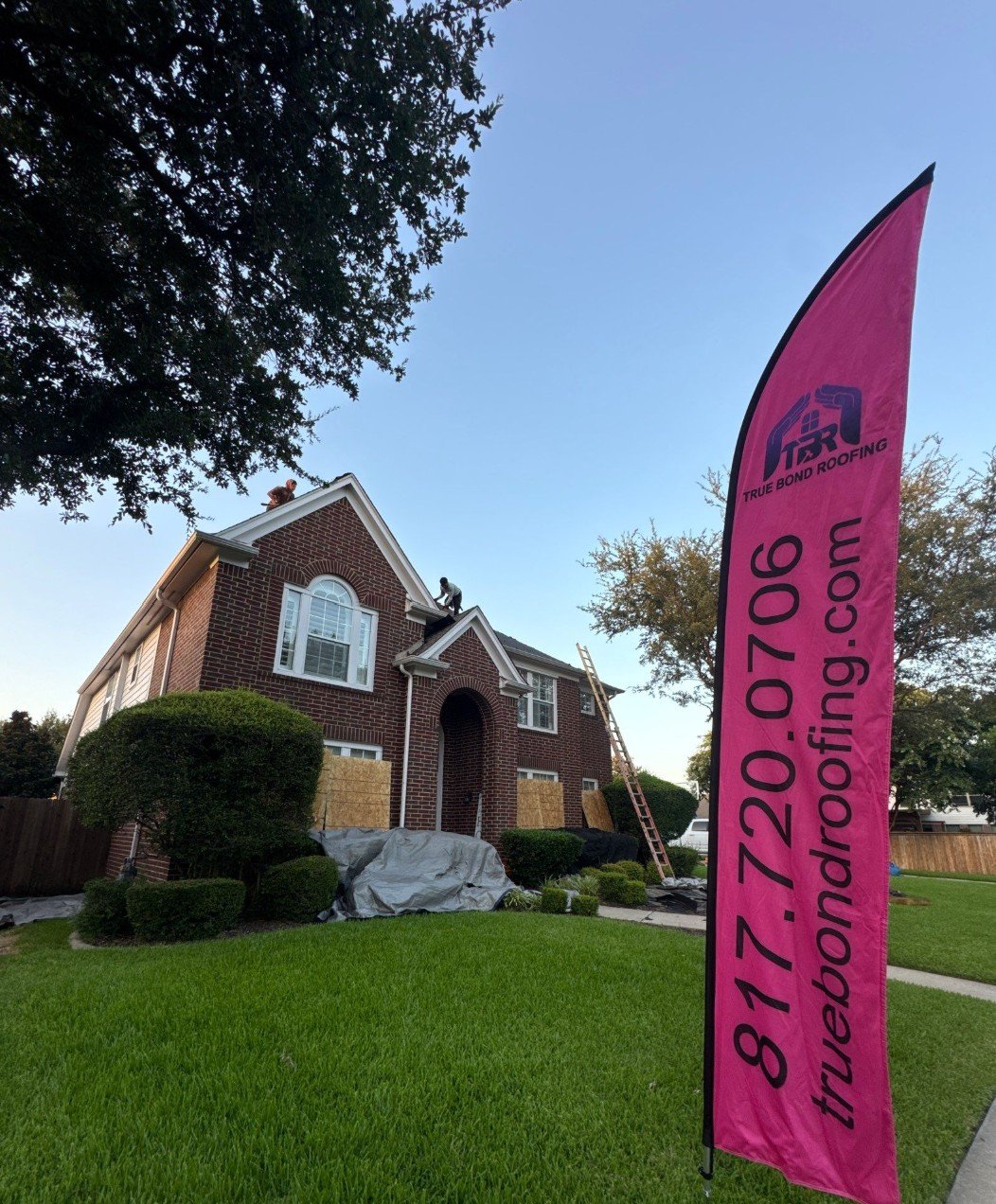 True Bond Roofing crew working on a residential roof replacement with company signage displayed at the job site.