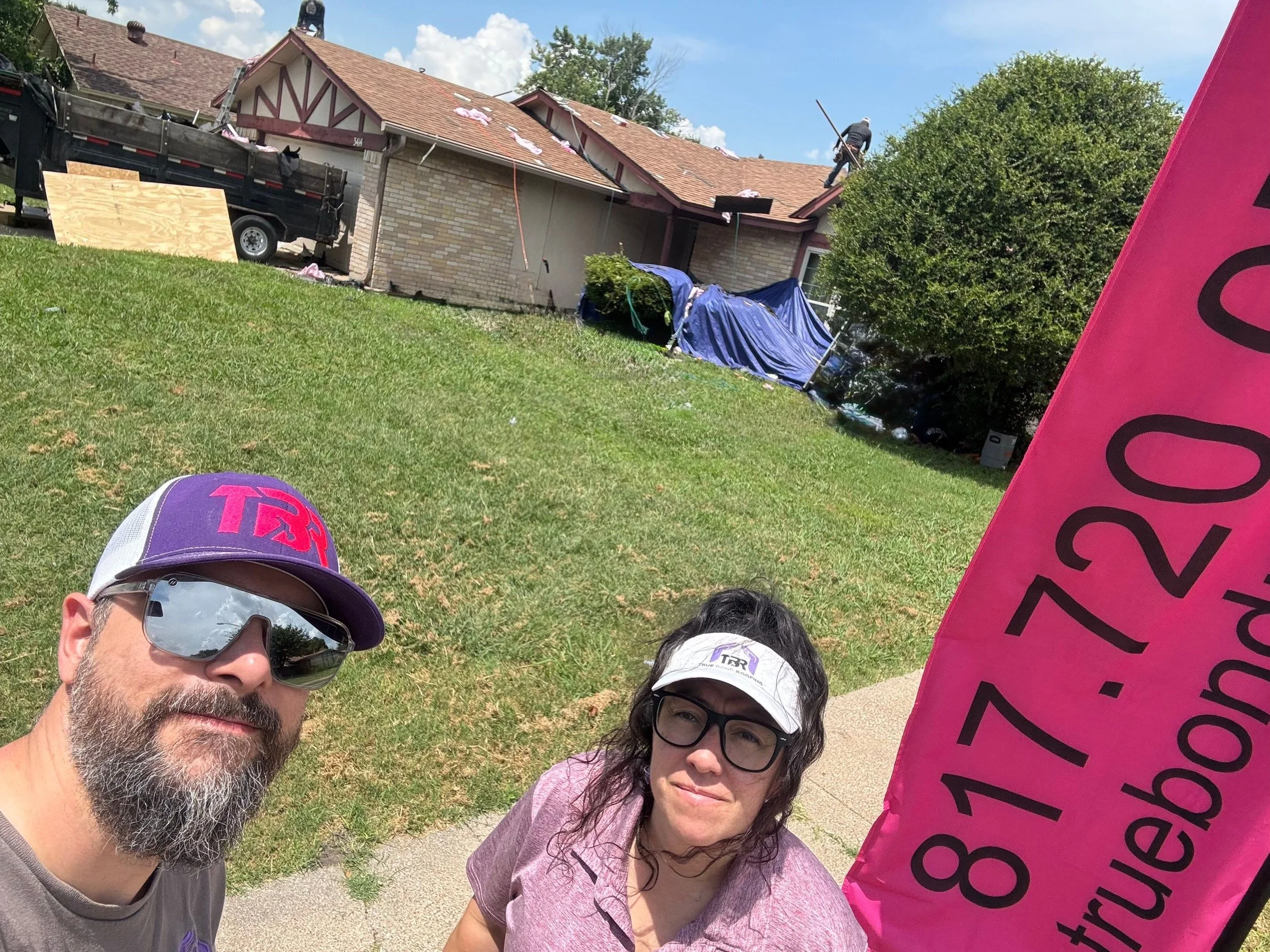 Aaron and Tiffany Lemons of True Bond Roofing at a residential roof installation, with their roofing crew working in the background.