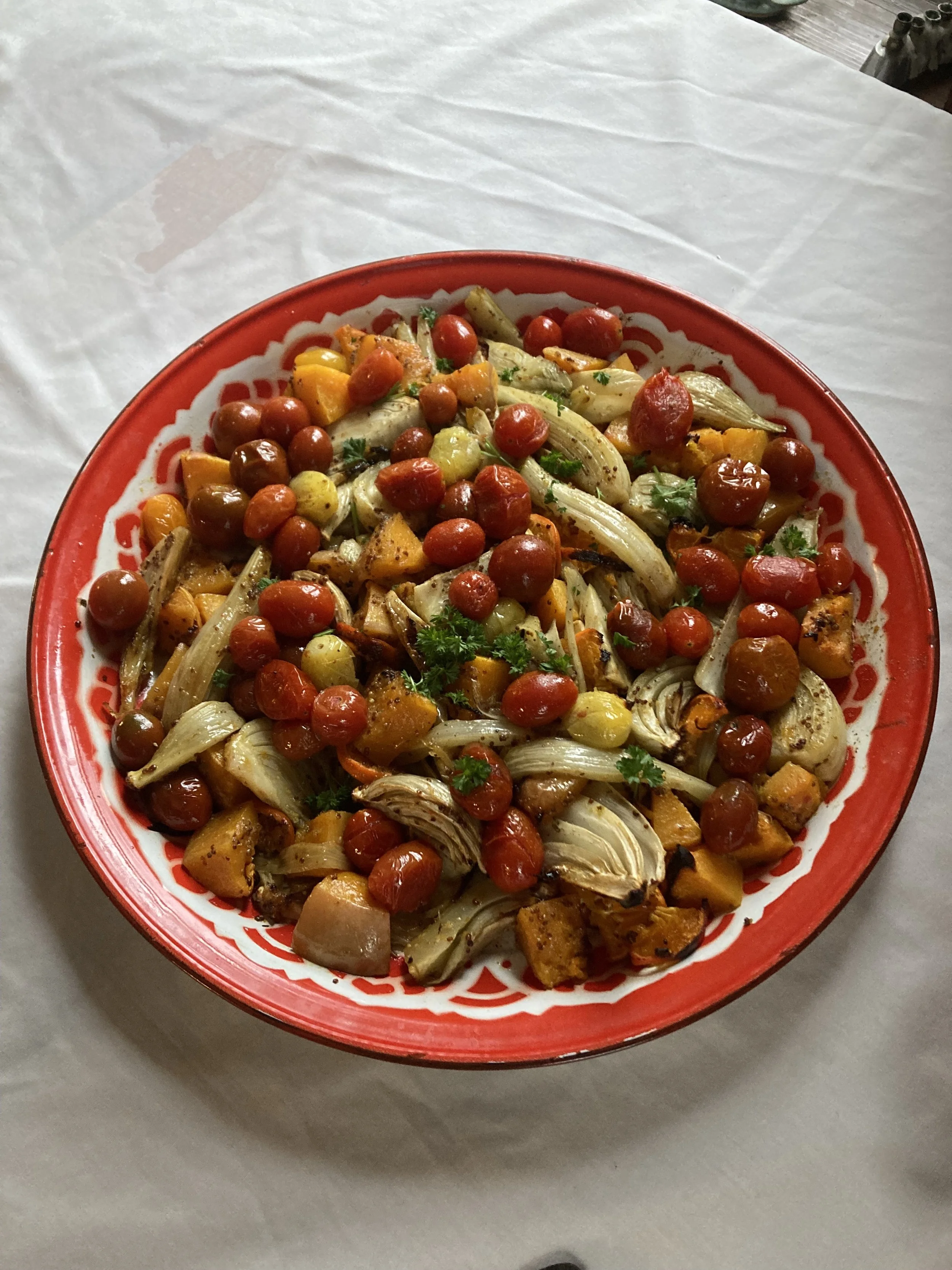 Roasted vegetable salad in a decorative red and white bowl, featuring cherry tomatoes, artichoke hearts, and herbs.