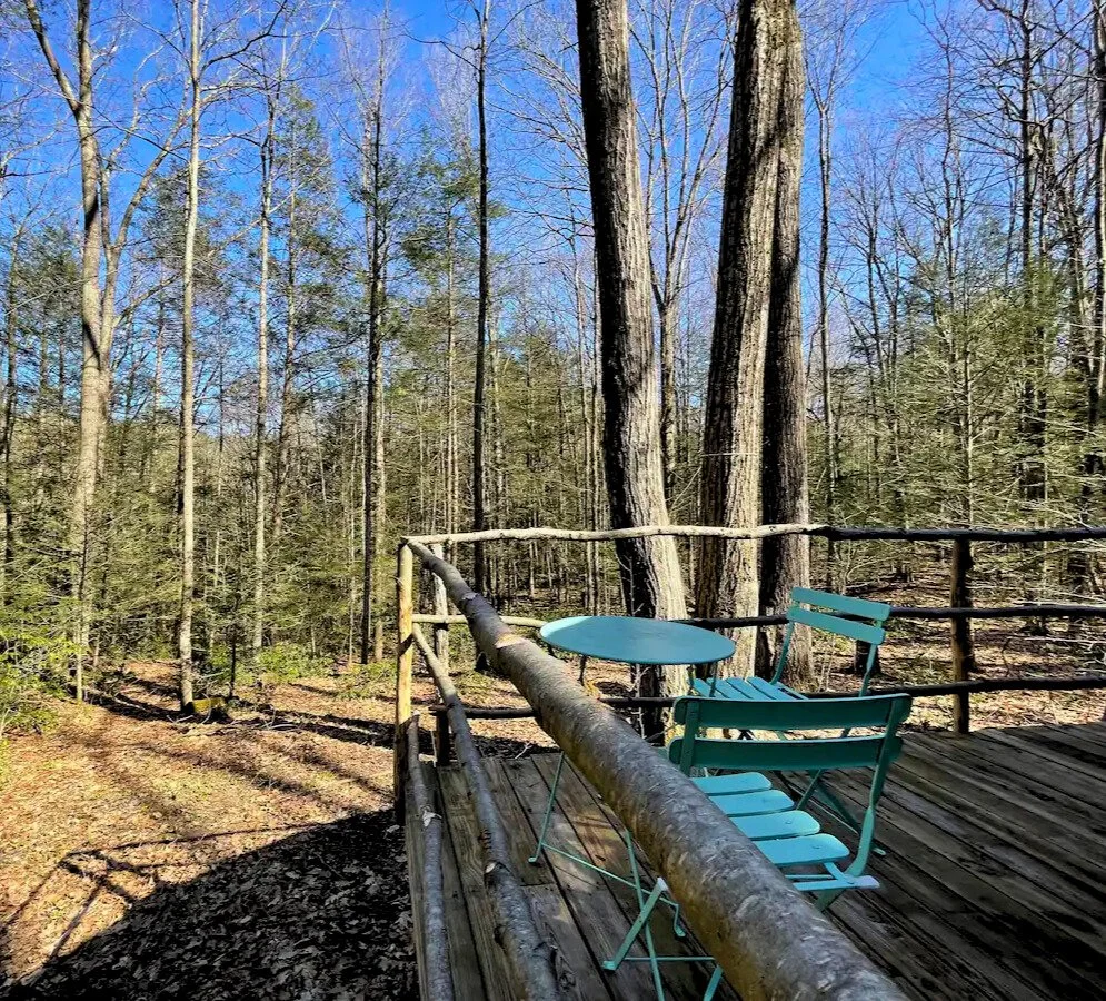 Wooden deck with a turquoise table and chairs overlooking a forest during daytime.
