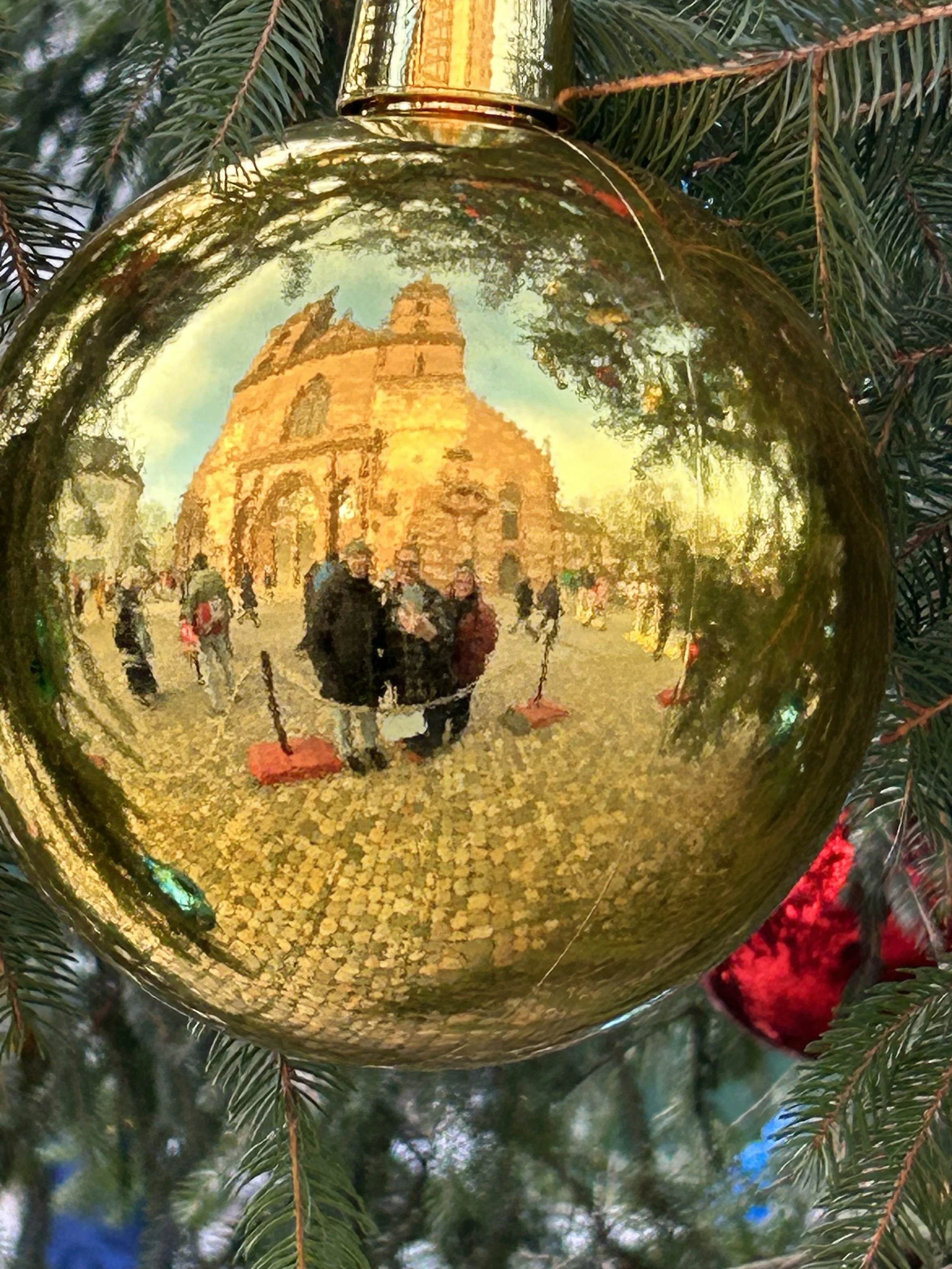 Reflection of a cathedral and Christmas market scene captured in a shiny gold ornament hanging on a decorated tree.
