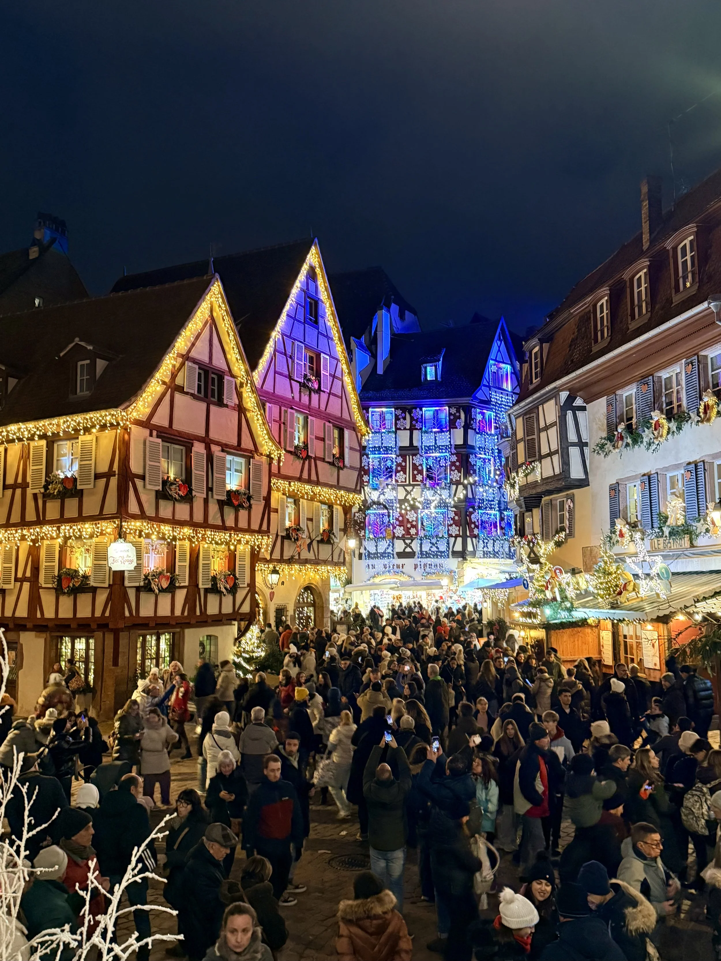 Crowds exploring the brightly lit half-timbered houses and festive stalls at the Colmar Christmas market at night