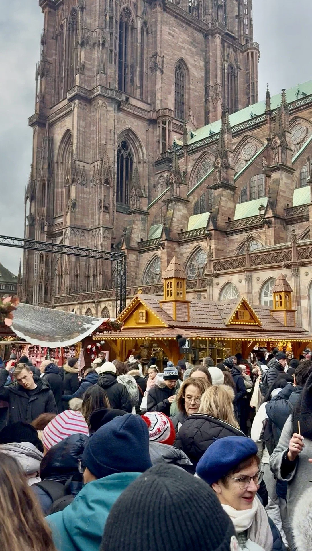 Image of Strasbourg’s massive Gothic cathedral towering over a packed Christmas market, with wooden stalls and bundled-up visitors filling the square.