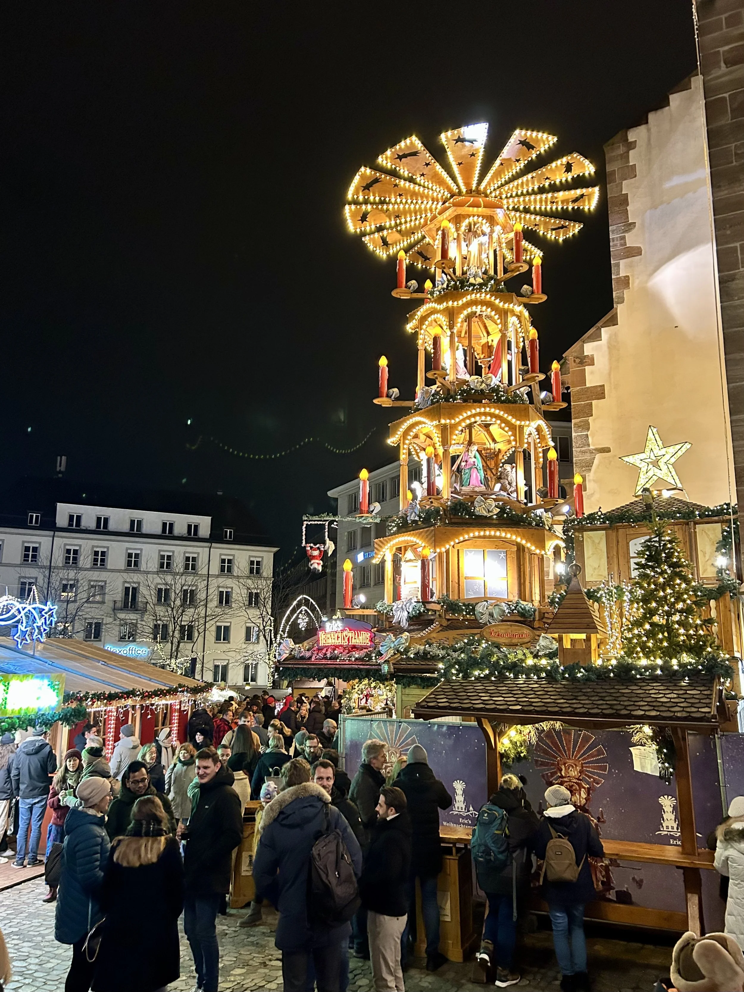 The Basel Minster towering over a festive carousel and Christmas market stalls as visitors walk the cobblestone square