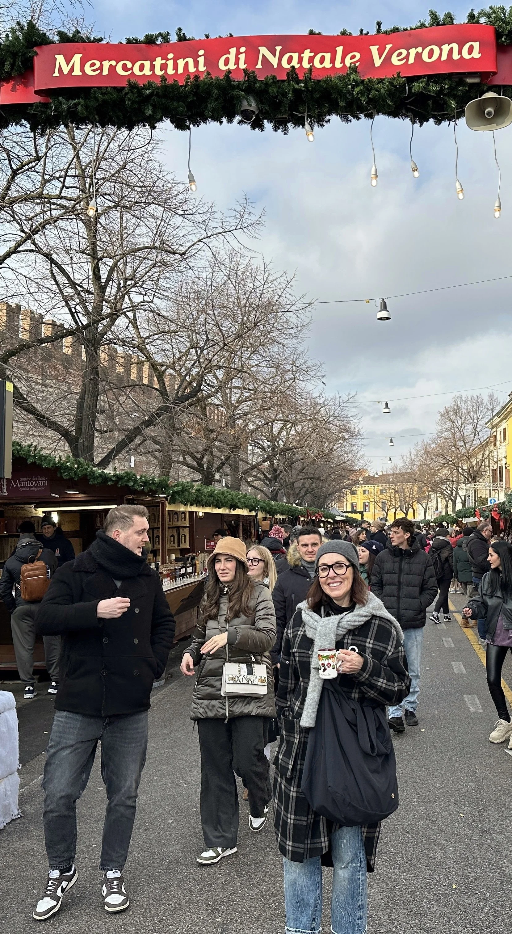 Crowds walking through the Verona Christmas Market under a red banner reading 'Mercatini di Natale Verona