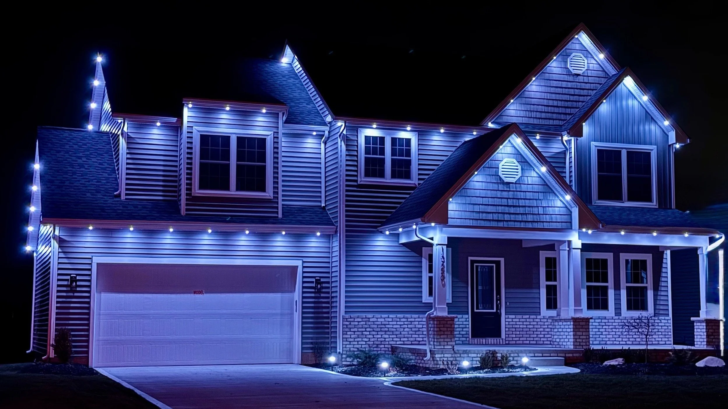 Night view of a two-story house decorated with blue and white Christmas lights.
