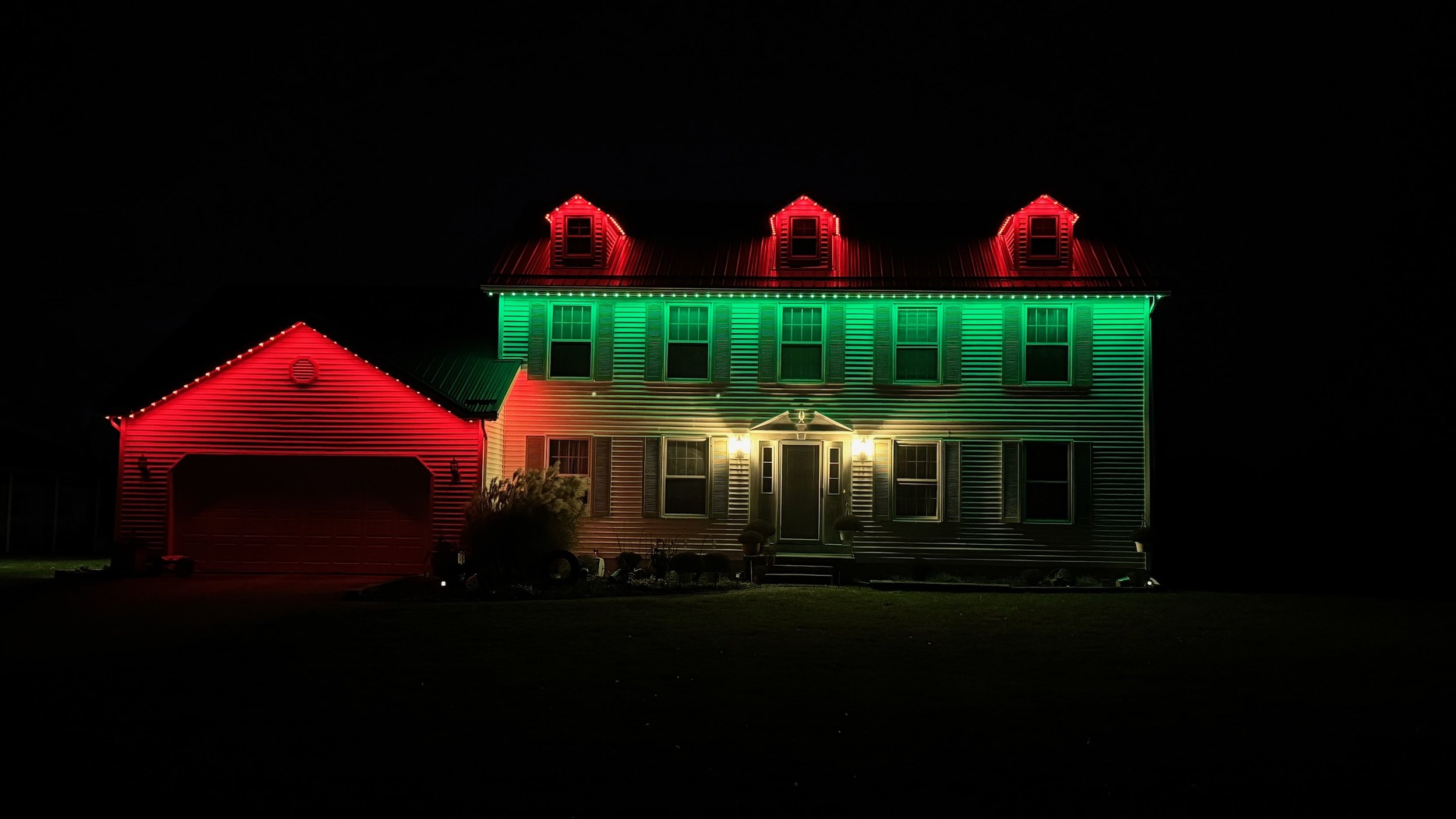 A house decorated with Christmas holiday lights at night, with red and green lights outlining the roof and windows.