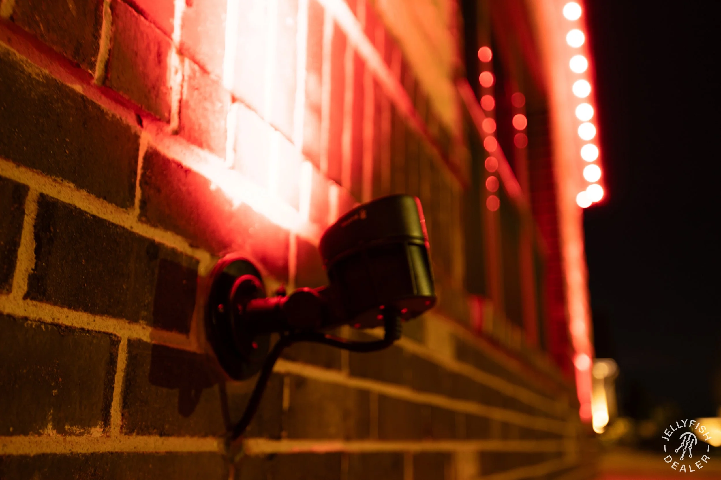 Close-up of a laser level projecting red lines on a brick wall at night, with a black cord and light attached.