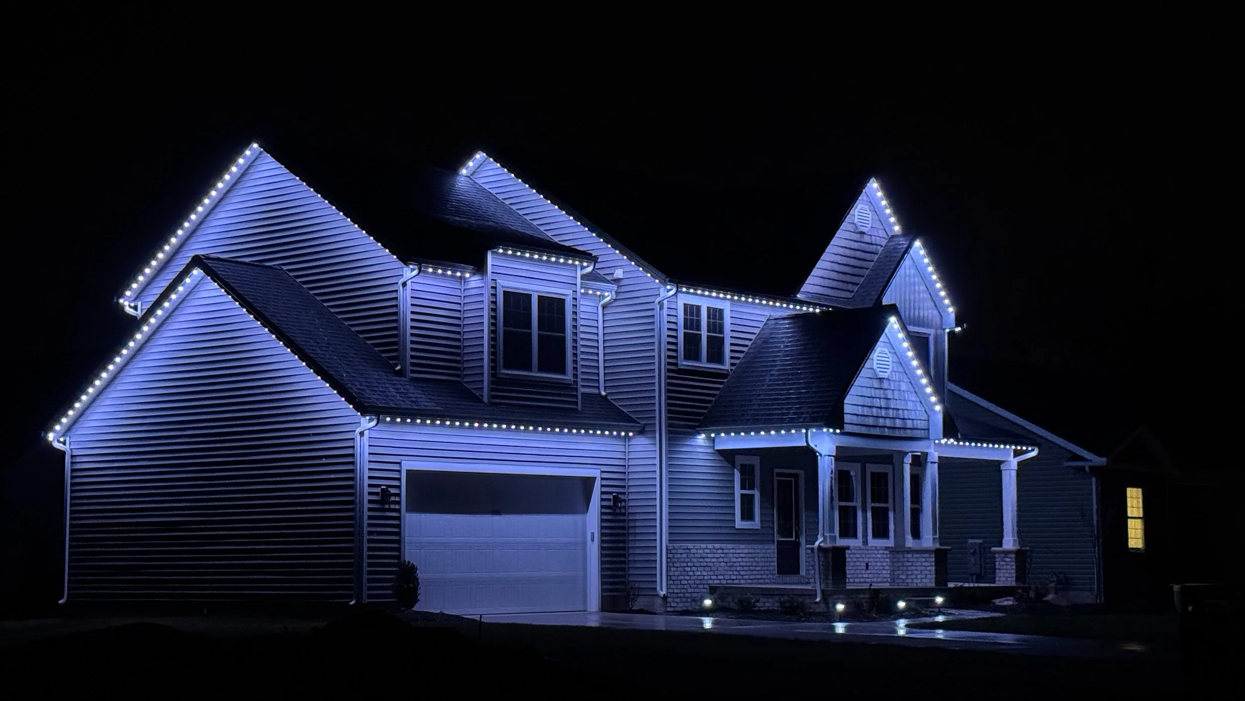 A large house at night decorated with white and blue string lights outlining the roof and windows.