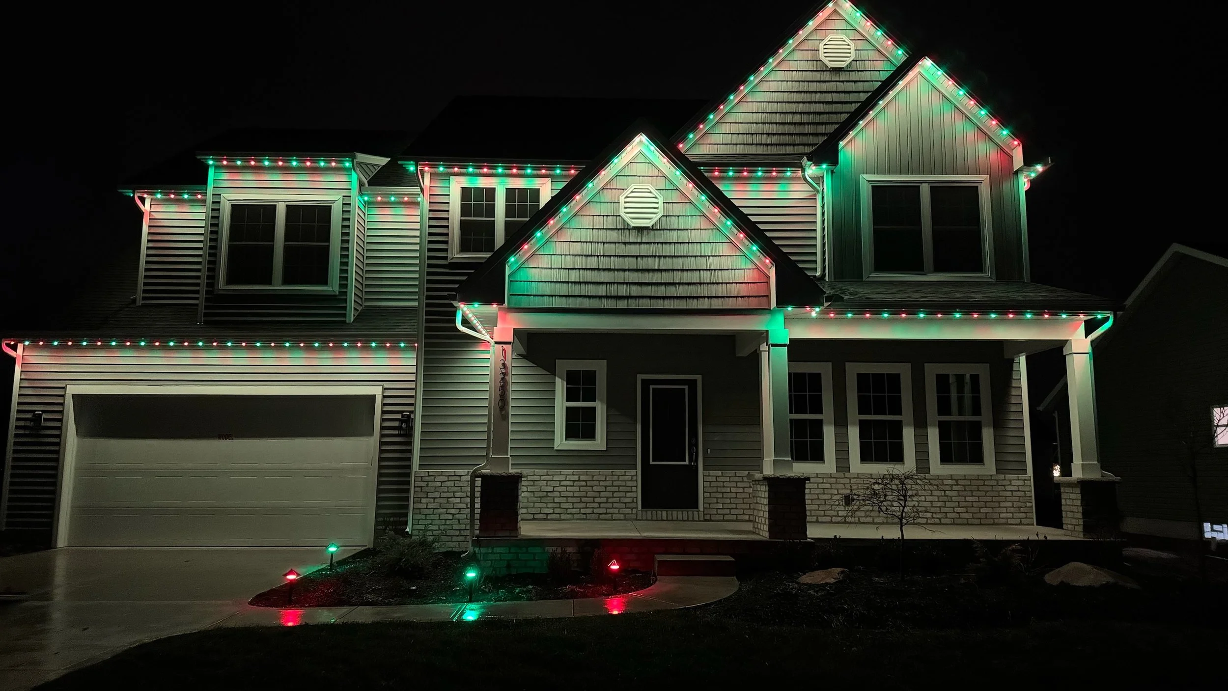 A two-story house decorated with multicolored Christmas lights at night.
