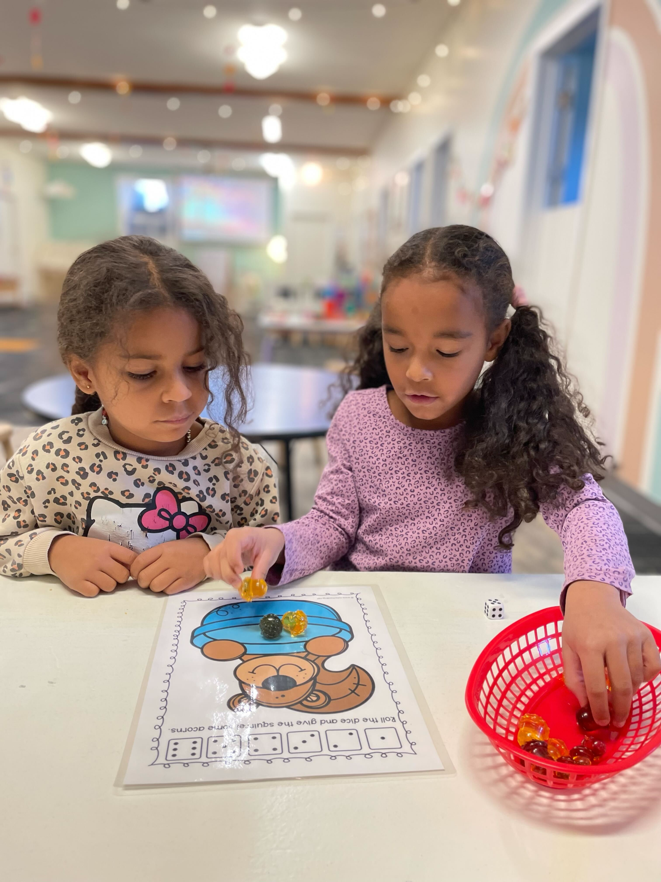 Two young girls playing a dice game at a table in a colorful room.