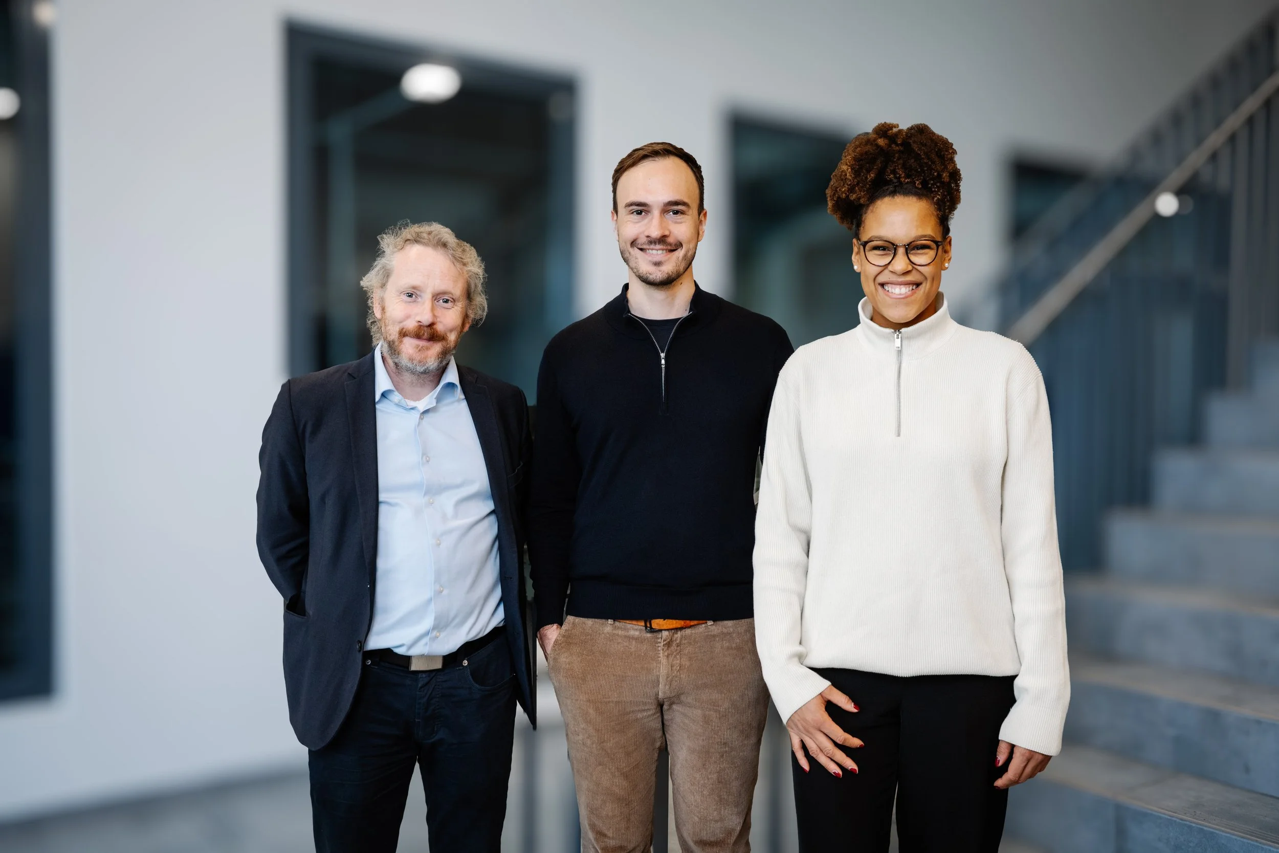 Three diverse professionals smiling in an office hallway.