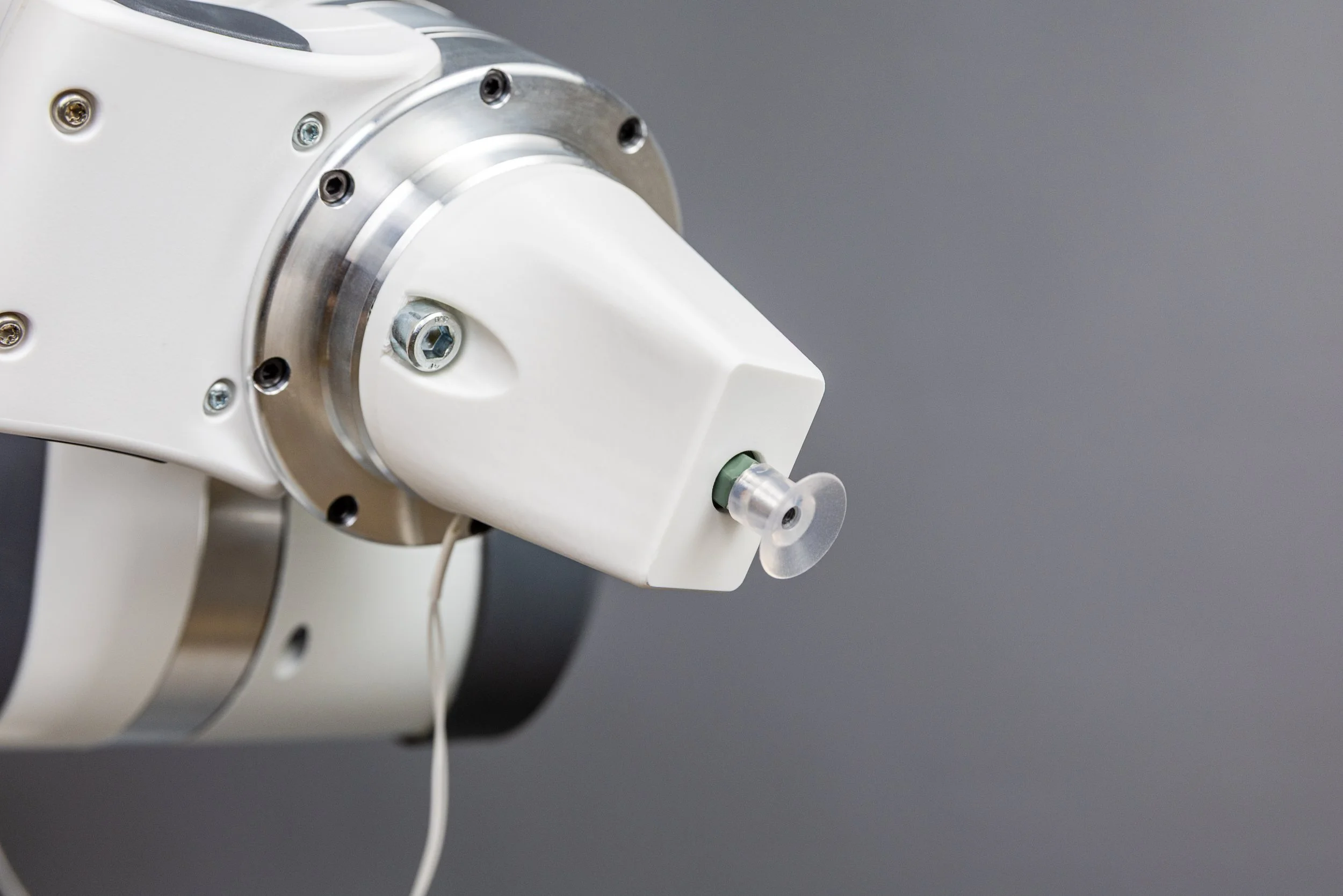 Close-up of a robotic surgical instrument or medical device with a white and metallic body against a gray background.
