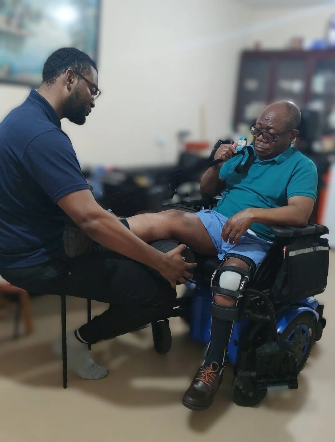 A Rehabilotation therapiest is doing guided exercises with an elderly man in a wheelchair in a home setting