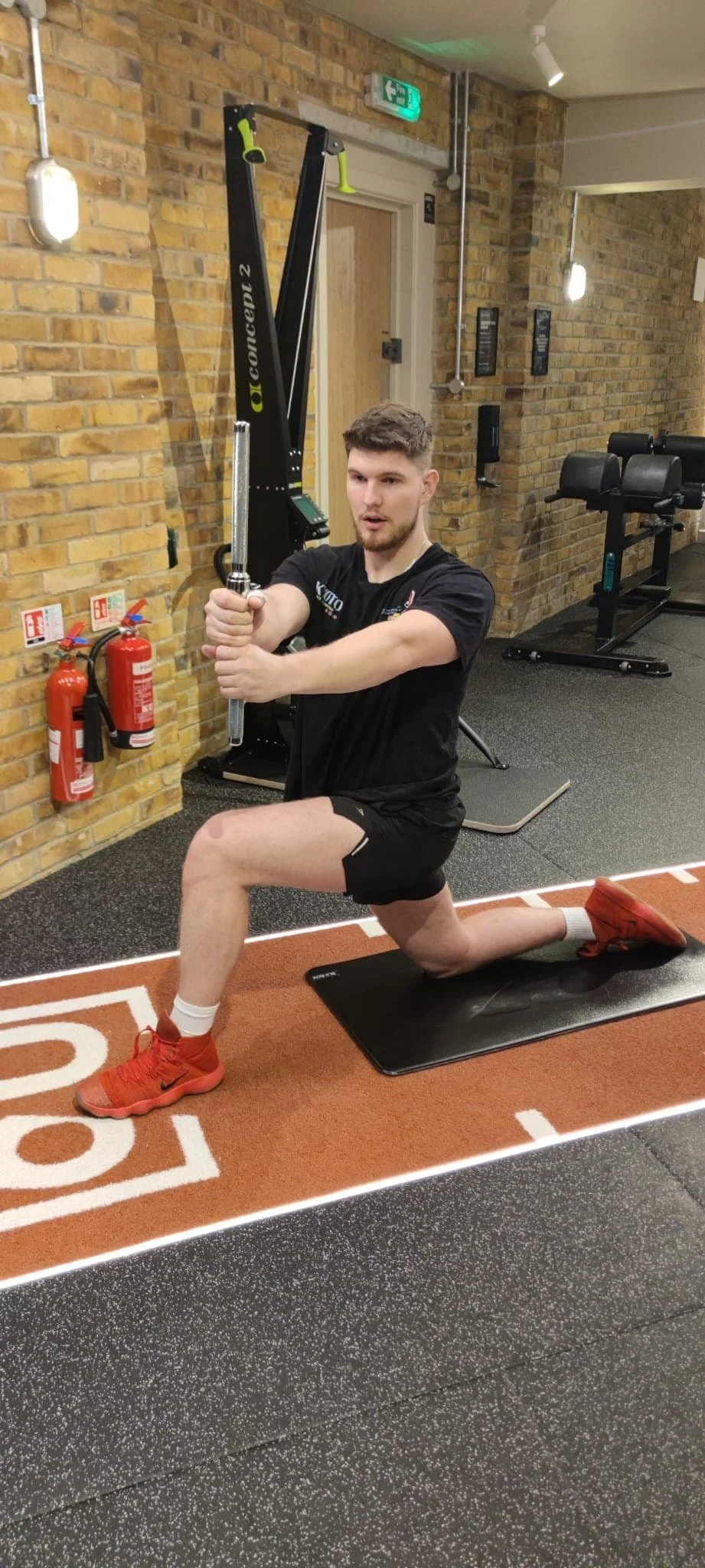 Man lunging with arm extended holding a weighted metal bar in gym setting