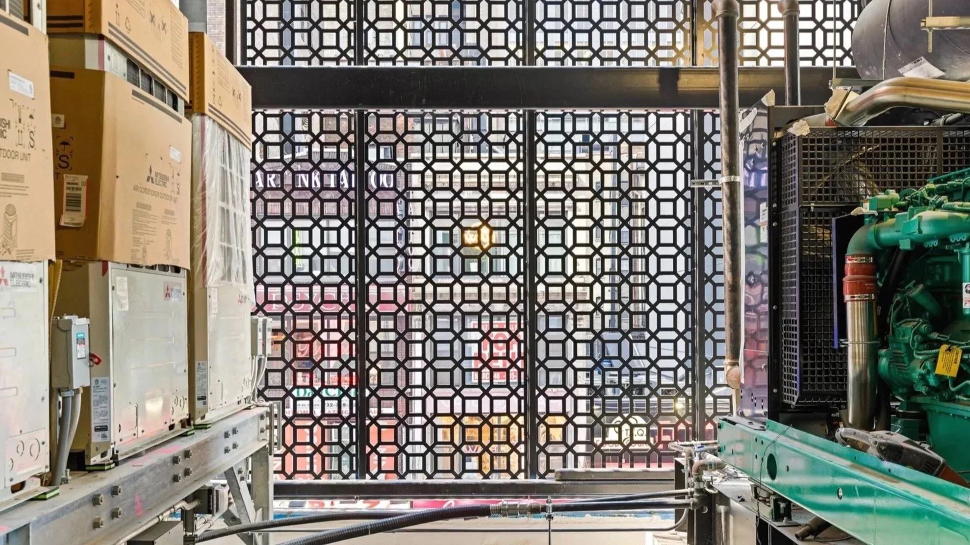 View from inside a building under construction, showing a decorative metal lattice facade with city buildings visible beyond.