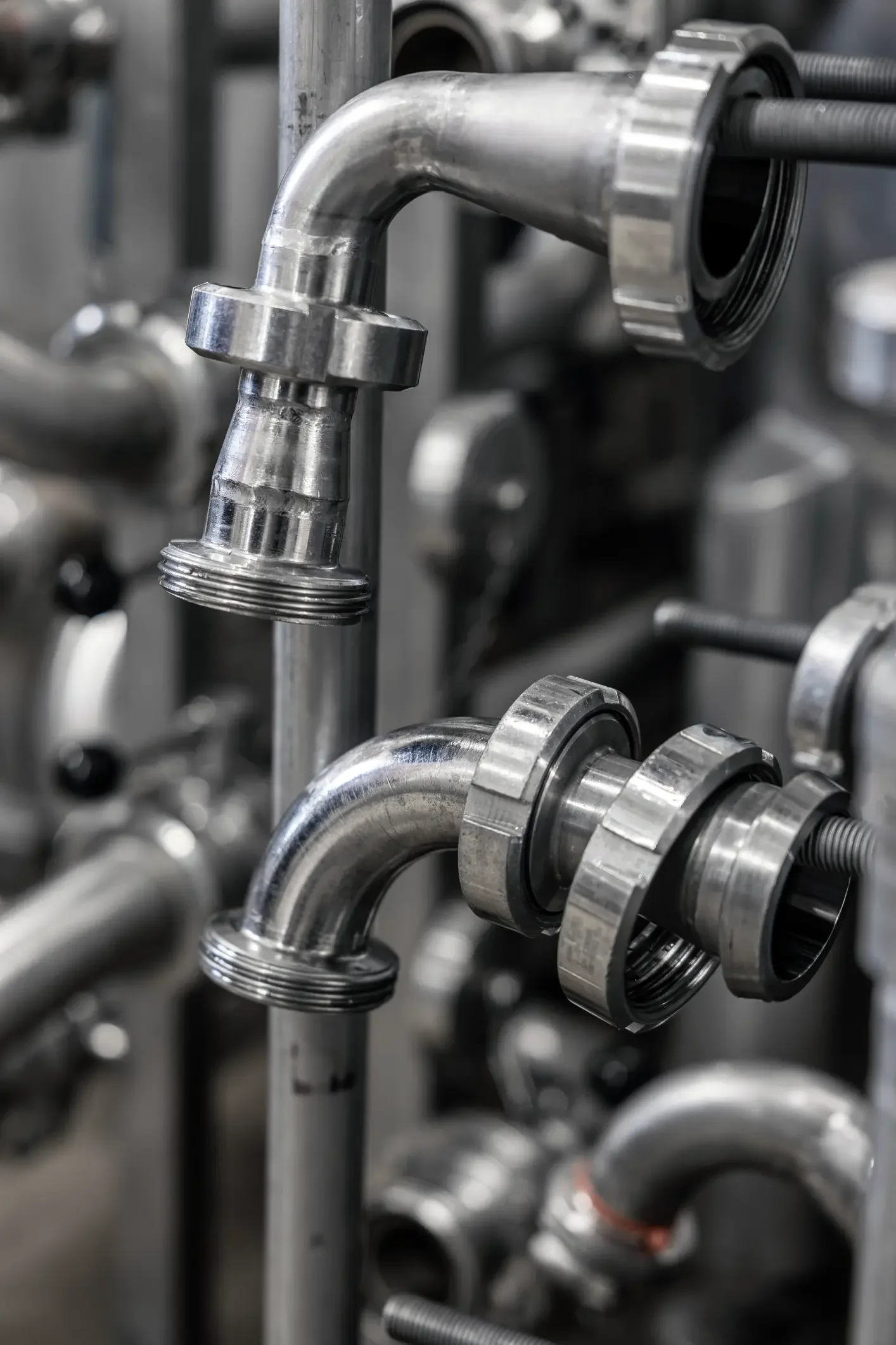 Close-up of industrial stainless steel pipes, elbow joints, and metal couplings in a manufacturing or processing plant.
