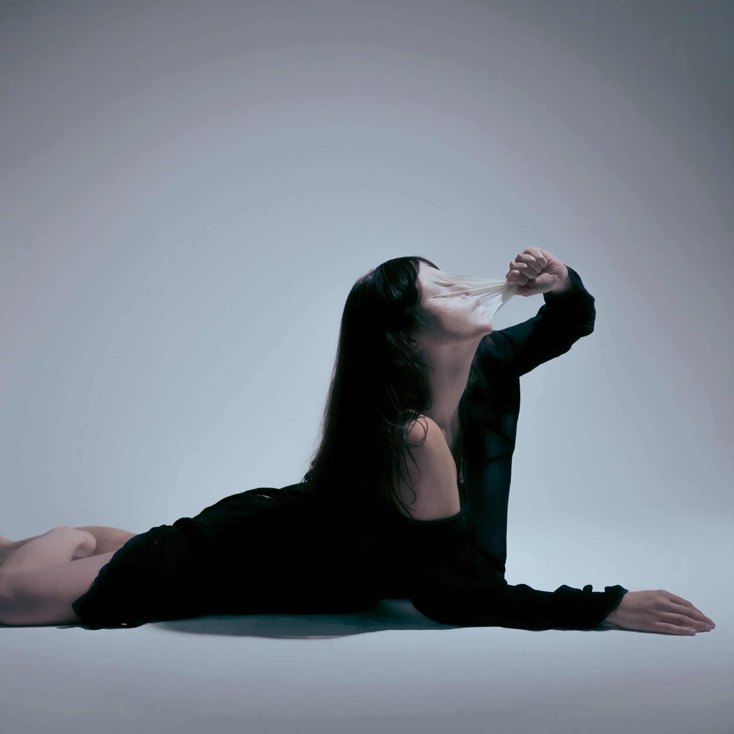 A woman performing a yoga pose on the floor, stretching her head backward and pulling her face with her hand.