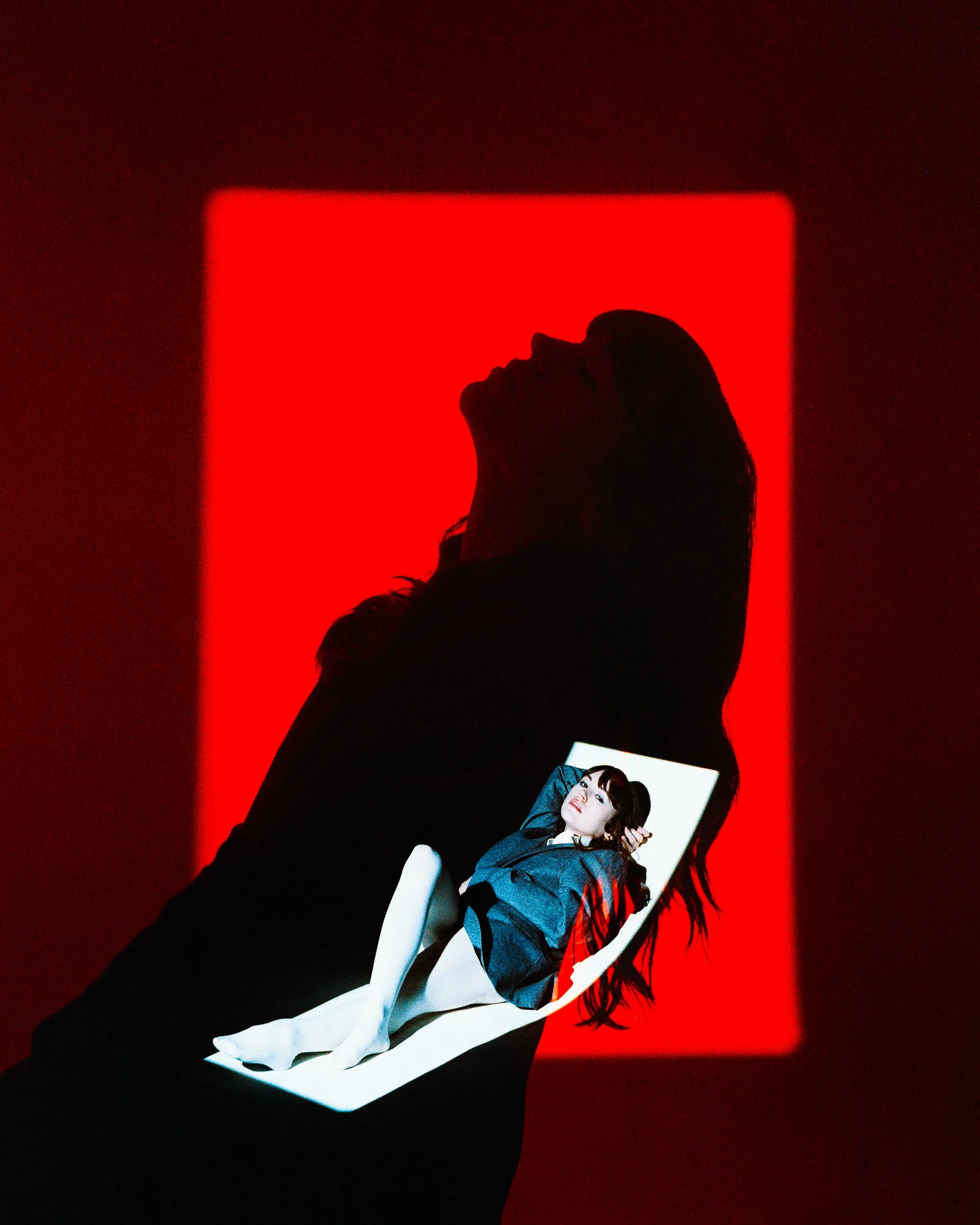 A silhouette of a person holding a photograph of a woman in a blue jacket, with a red light in the background.