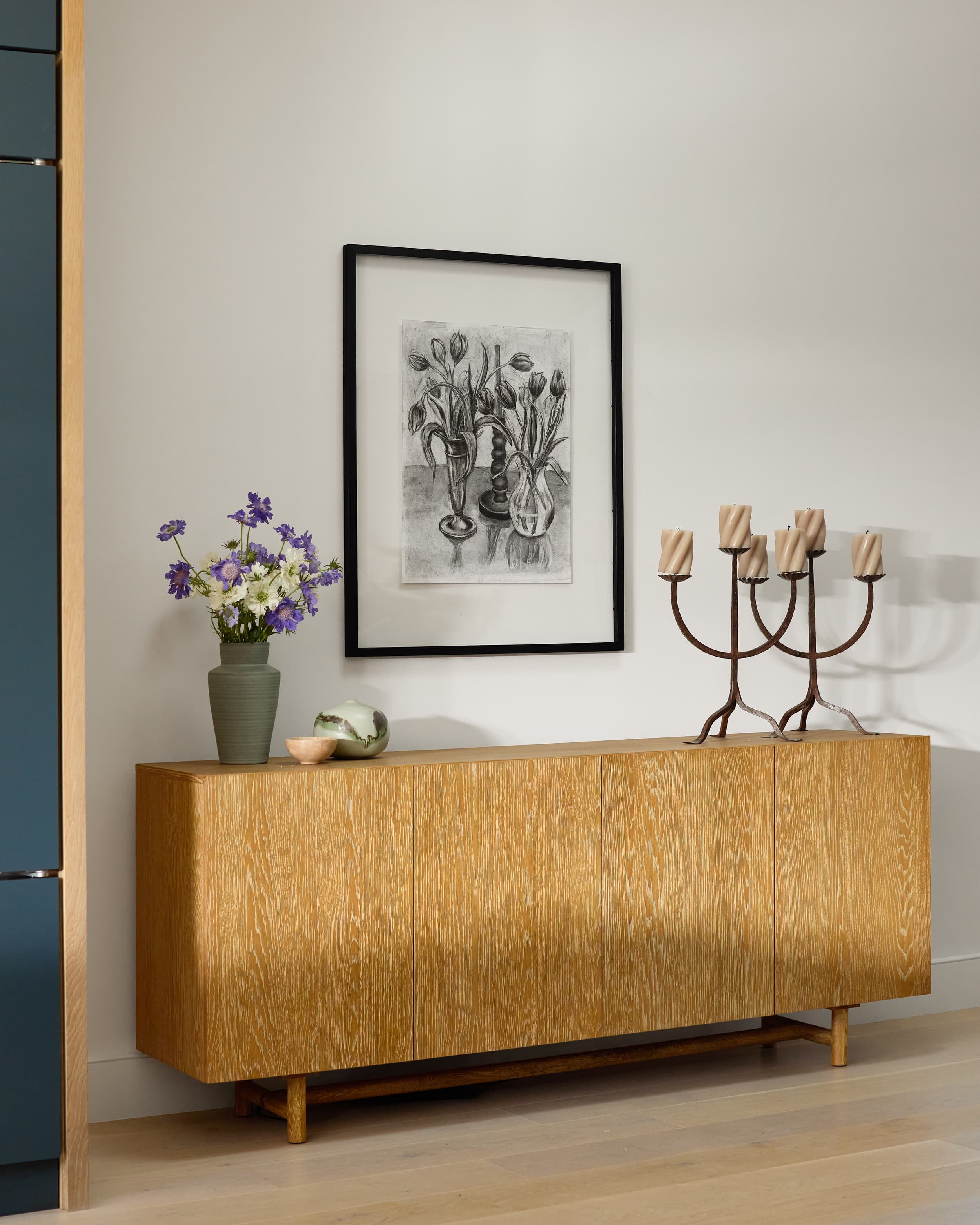 White oak sideboard styled with a framed tulip sketch, sculptural candelabra and purple flowers