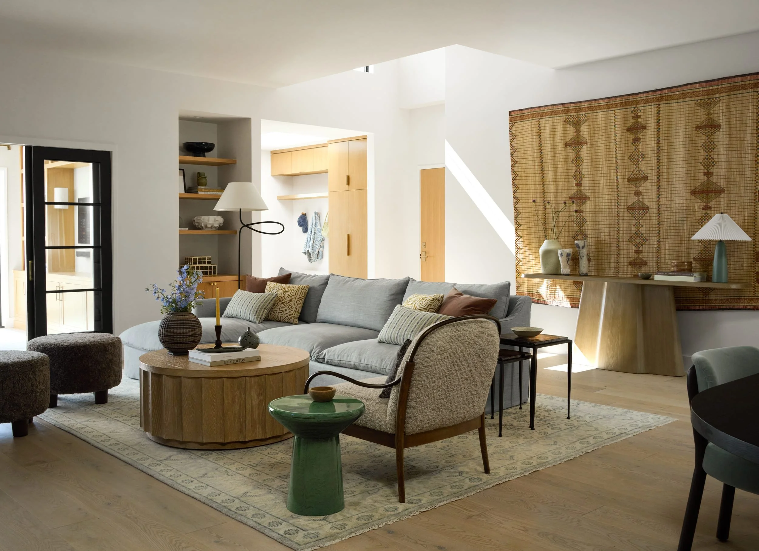 Living room with a light blue sectional, round wood coffee table, boucle armchair and vintage rug