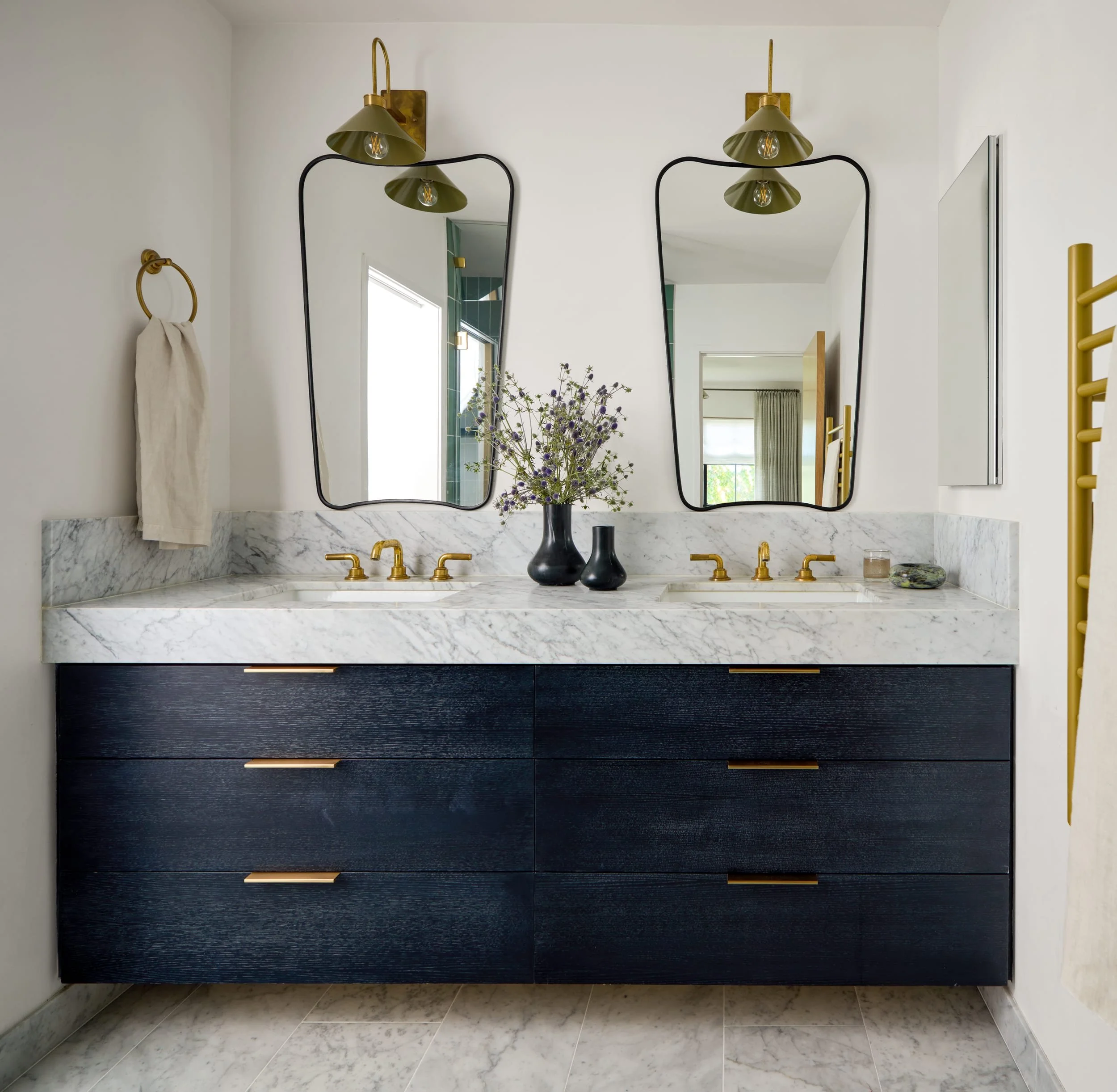 Bathroom with a navy oak double vanity, marble counter, brass faucets and arched mirrors