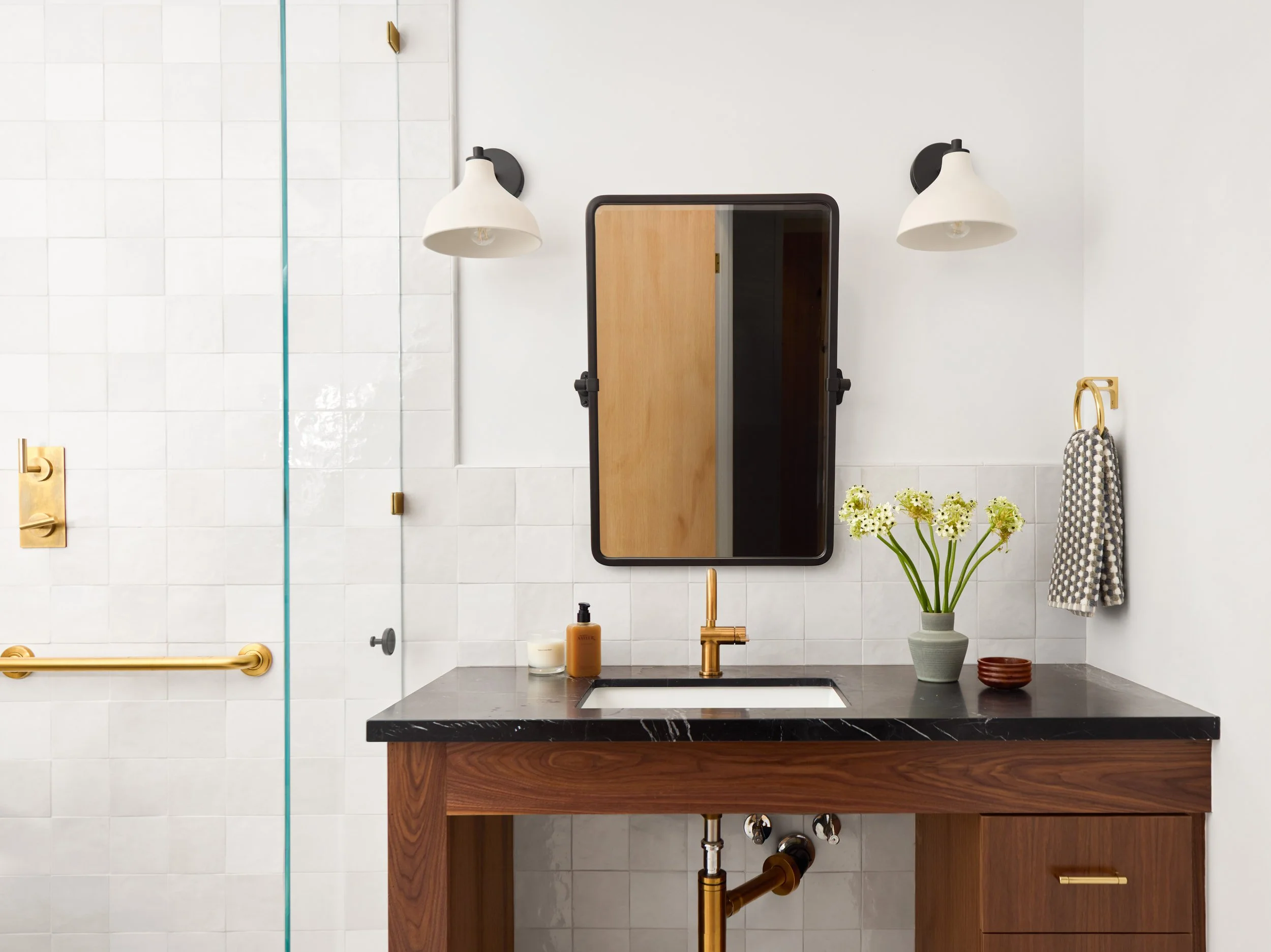 Accessible bathroom with a walnut vanity, black stone counter, brass grab bar and white tile walls