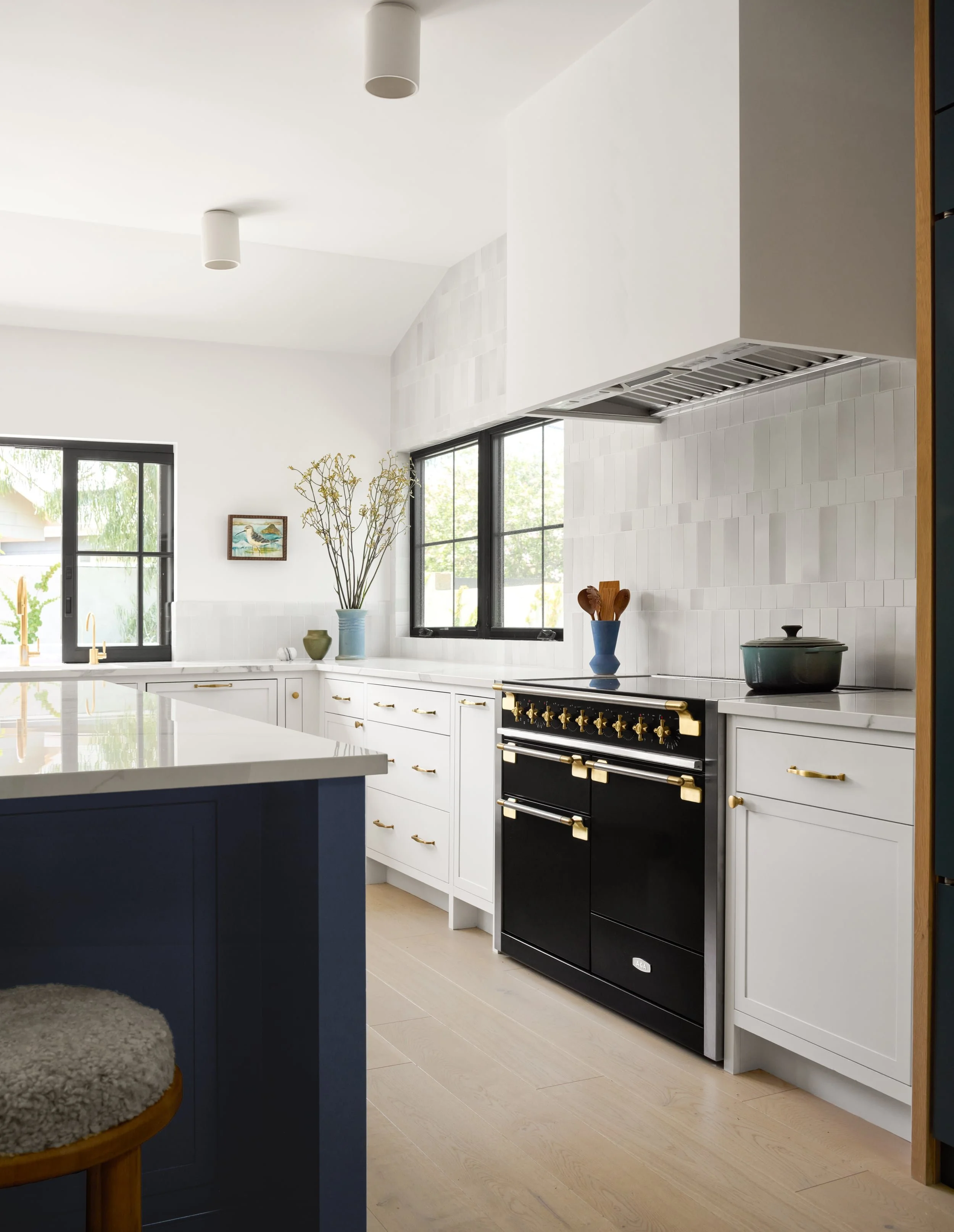 White kitchen with a black and brass range, plaster hood and handmade heath tile backsplash