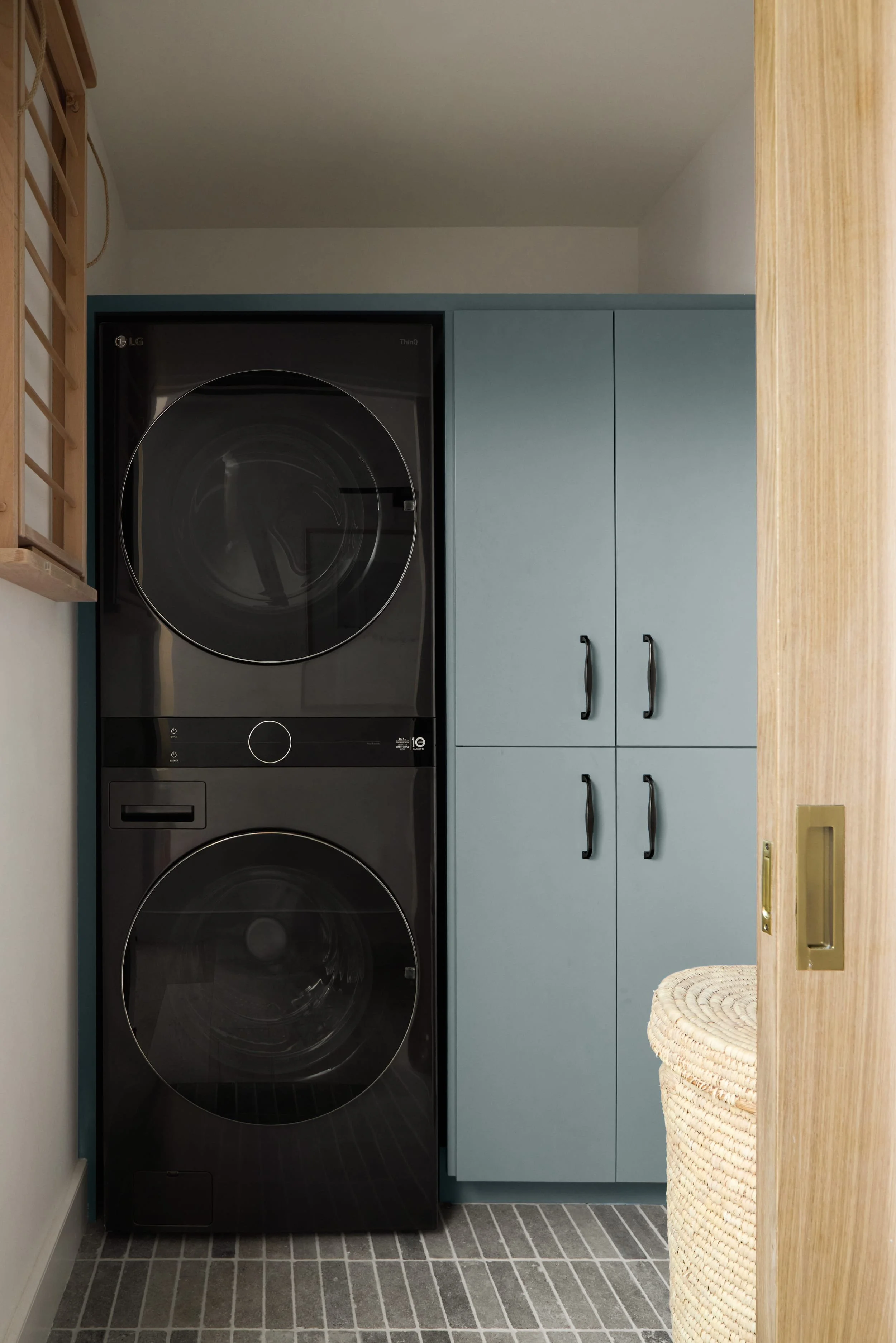 Laundry room with a stacked washer and dryer and pale blue cabinets behind an oak pocket door