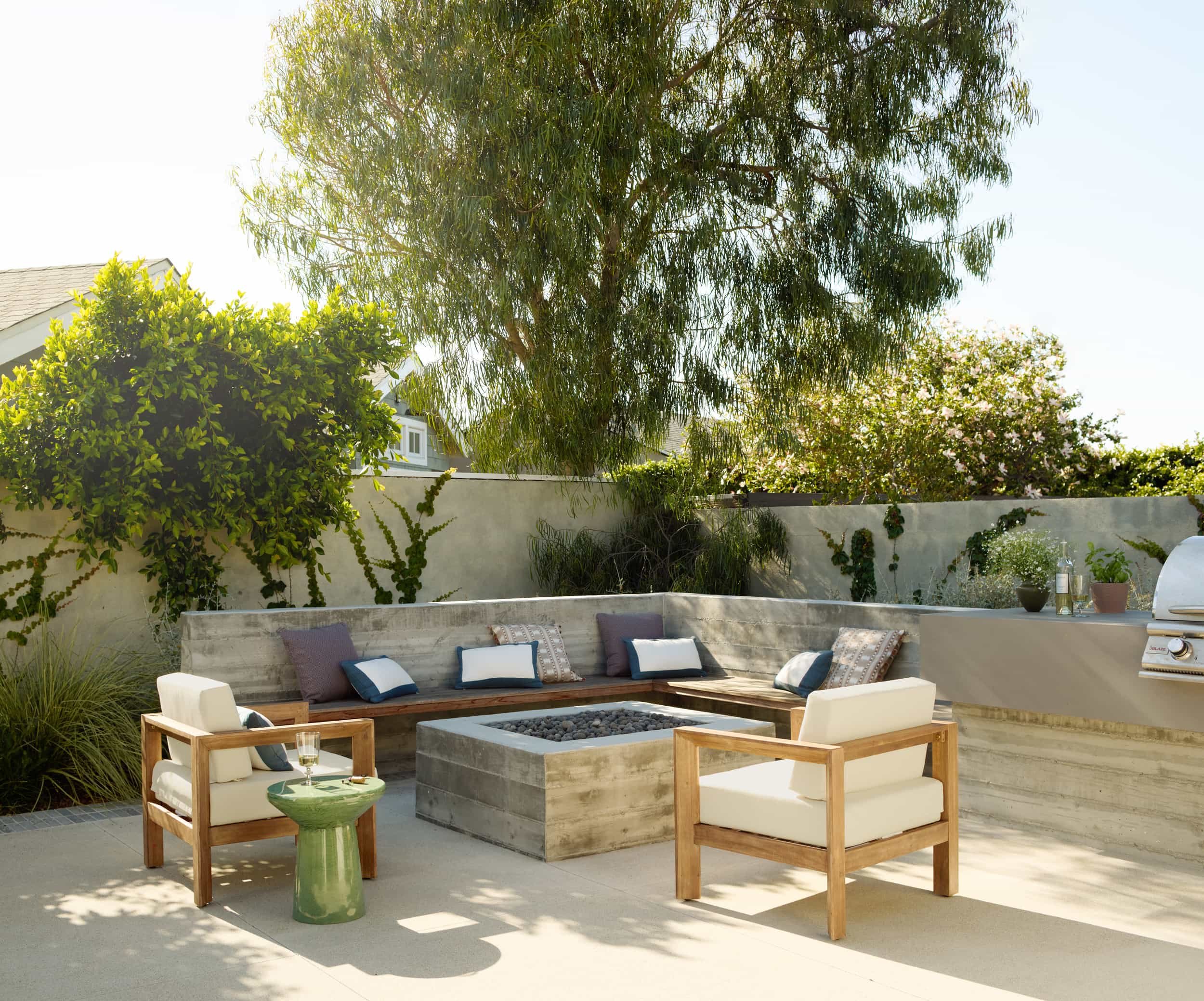 Backyard patio with a concrete fire pit, built-in bench seating and teak lounge chairs under a eucalyptus tree