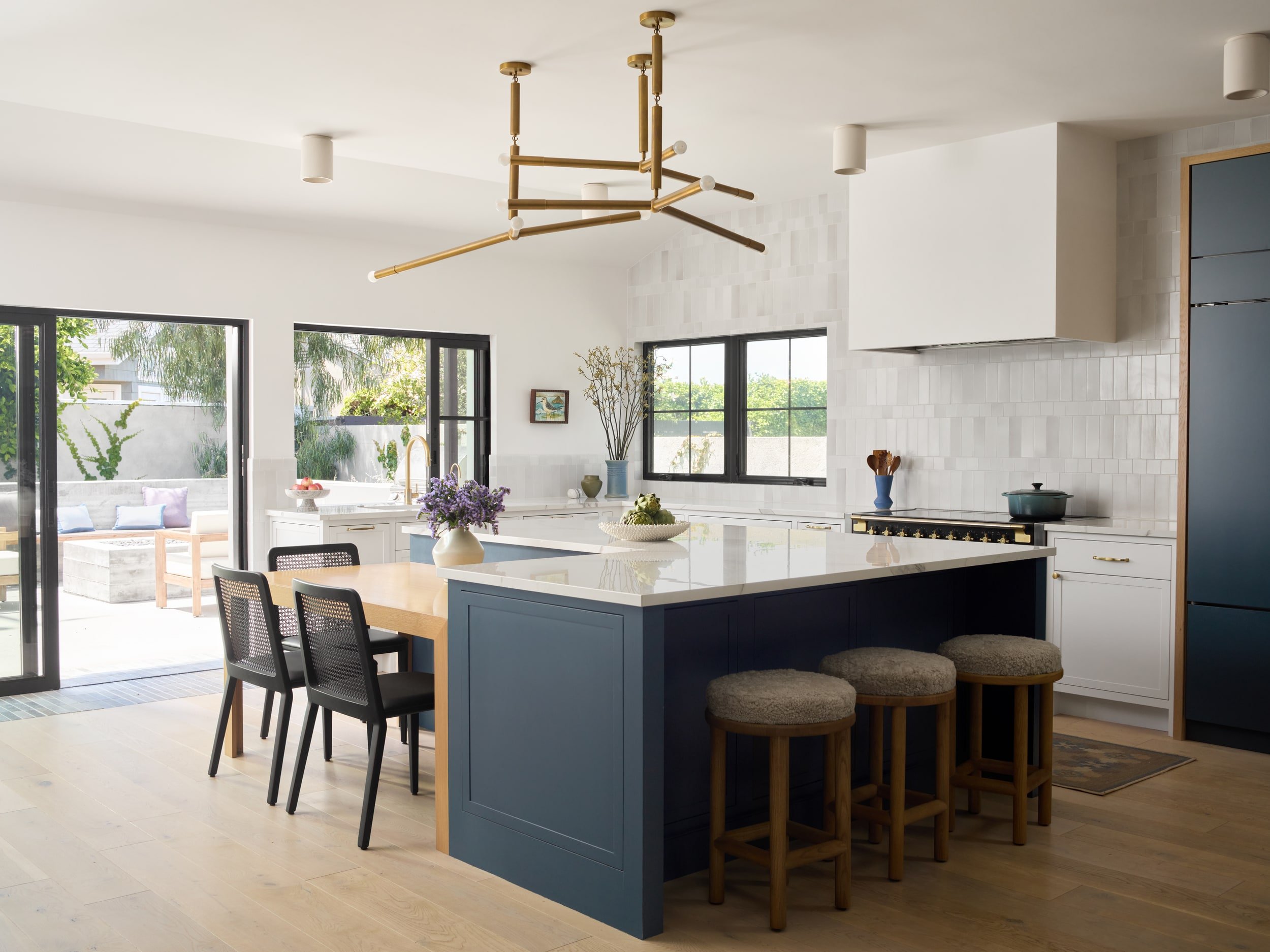 Navy kitchen island with white quartz counters, woven counter stools and an attached oak dining table