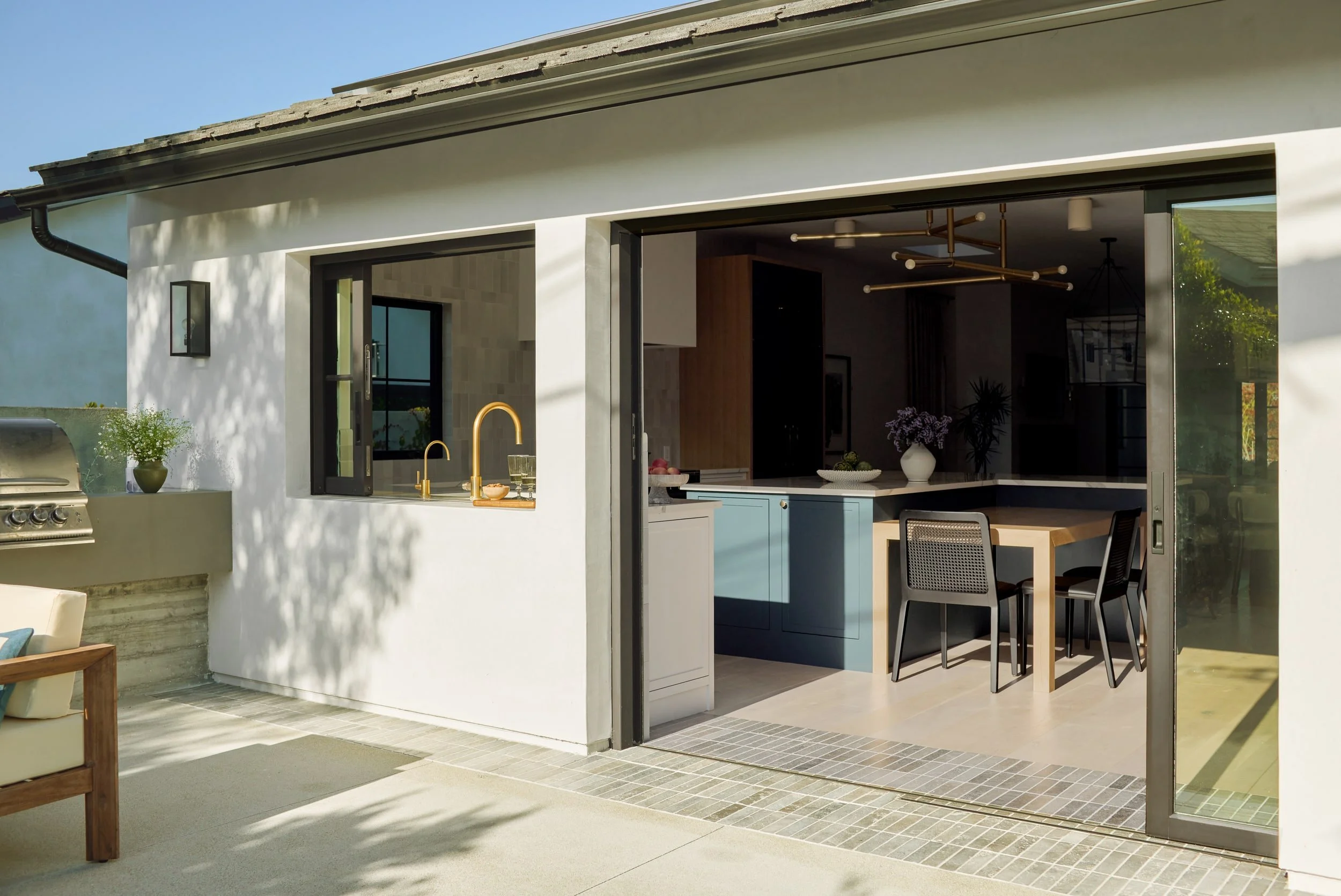 Sliding glass wall opening the kitchen to an outdoor patio with a built-in grill