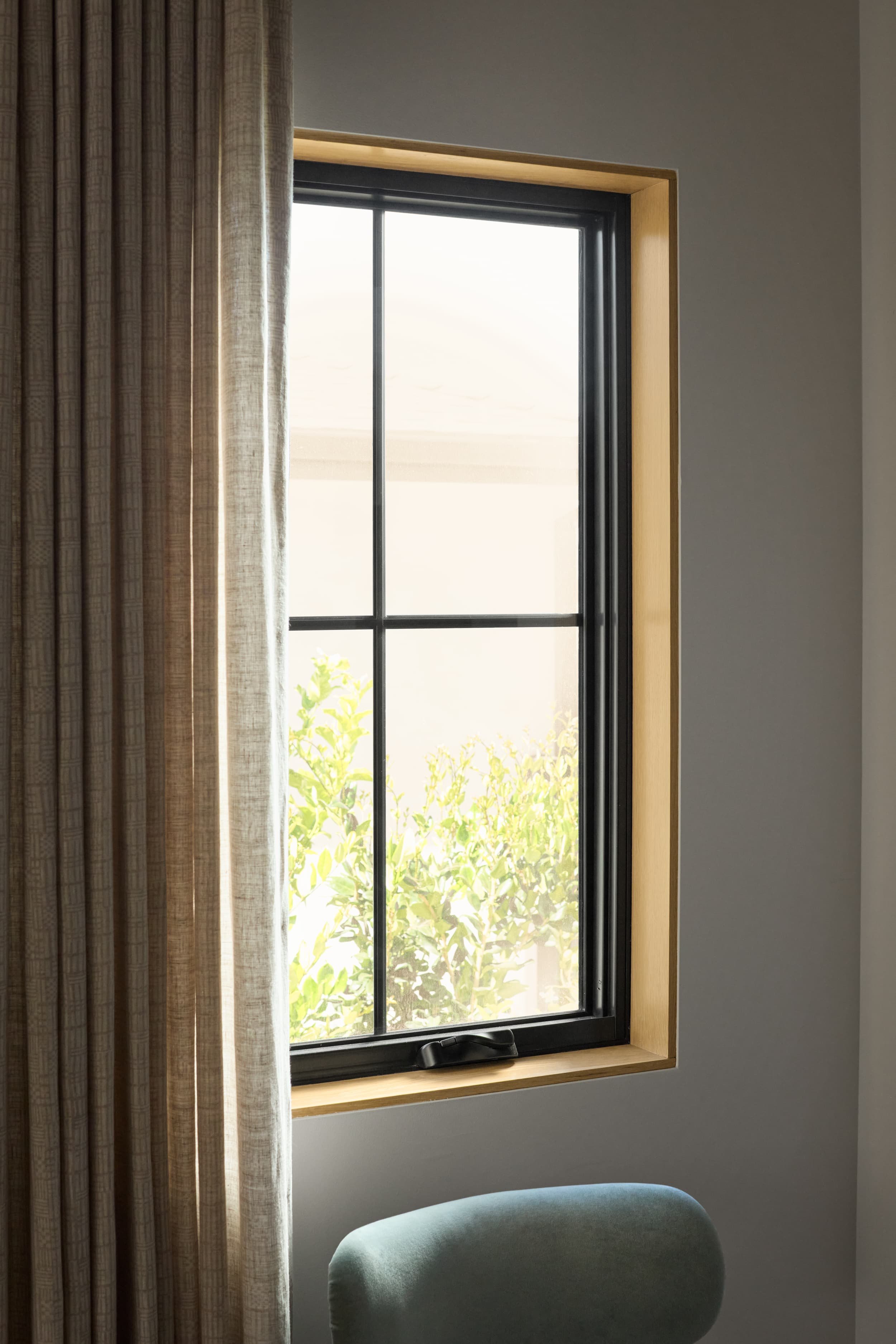 Black window with white oak trim, linen drapery and a sage green ottoman