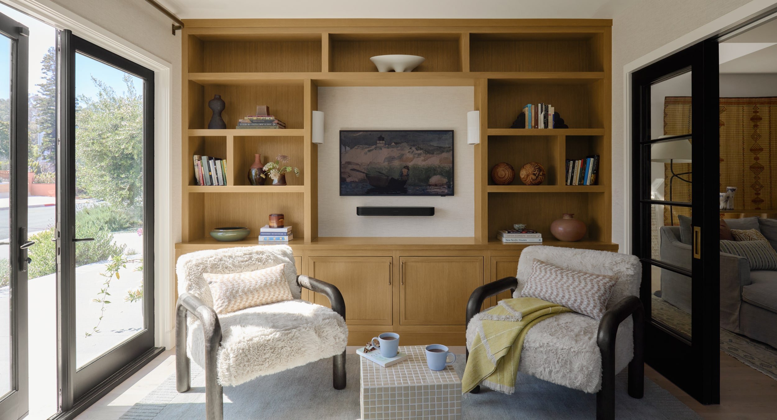 Cozy den with two shearling armchairs in front of white oak built-in shelving and a mounted TV