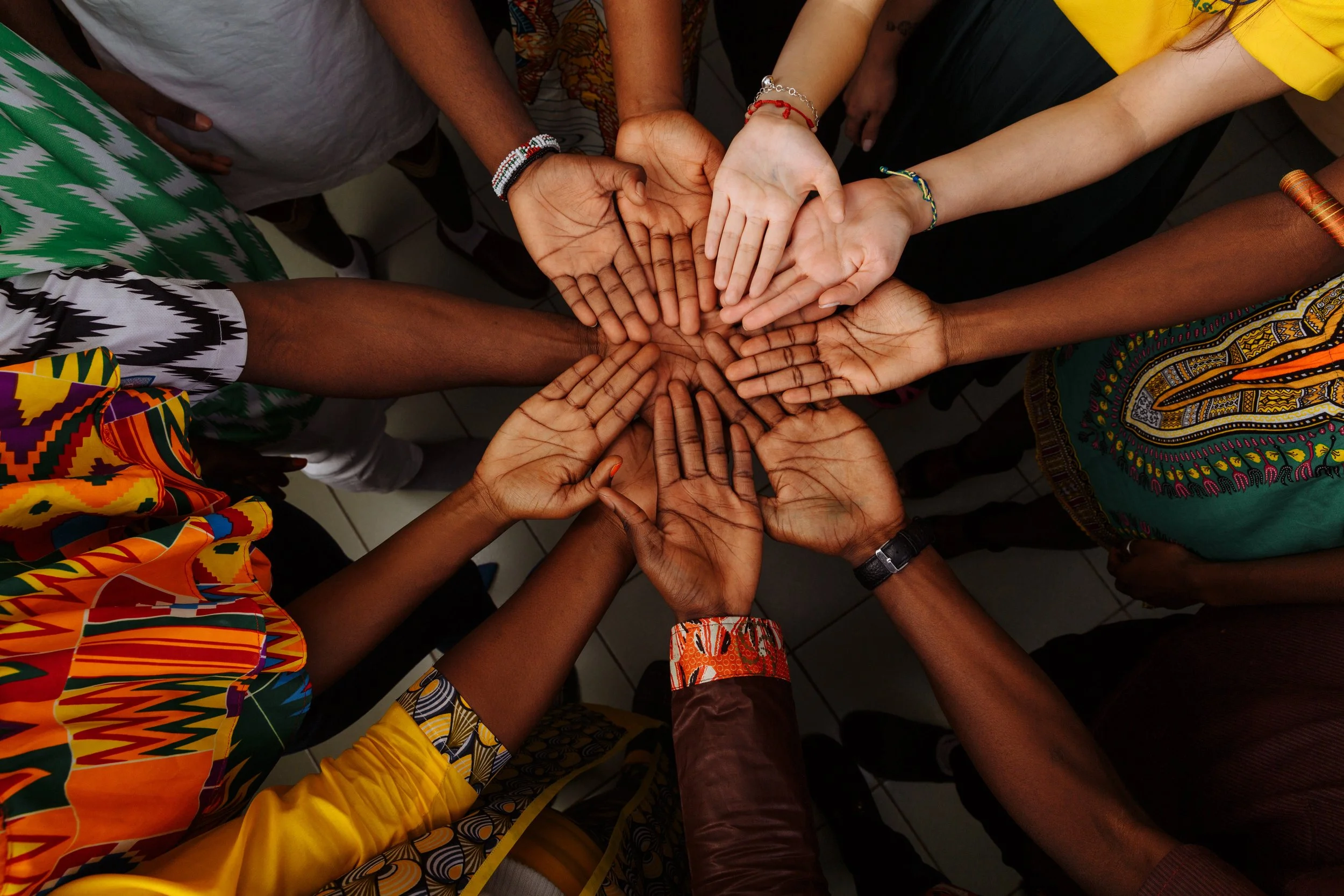 Multiple hands of diverse skin tones and ages stacked together in a circle, symbolizing unity and teamwork.