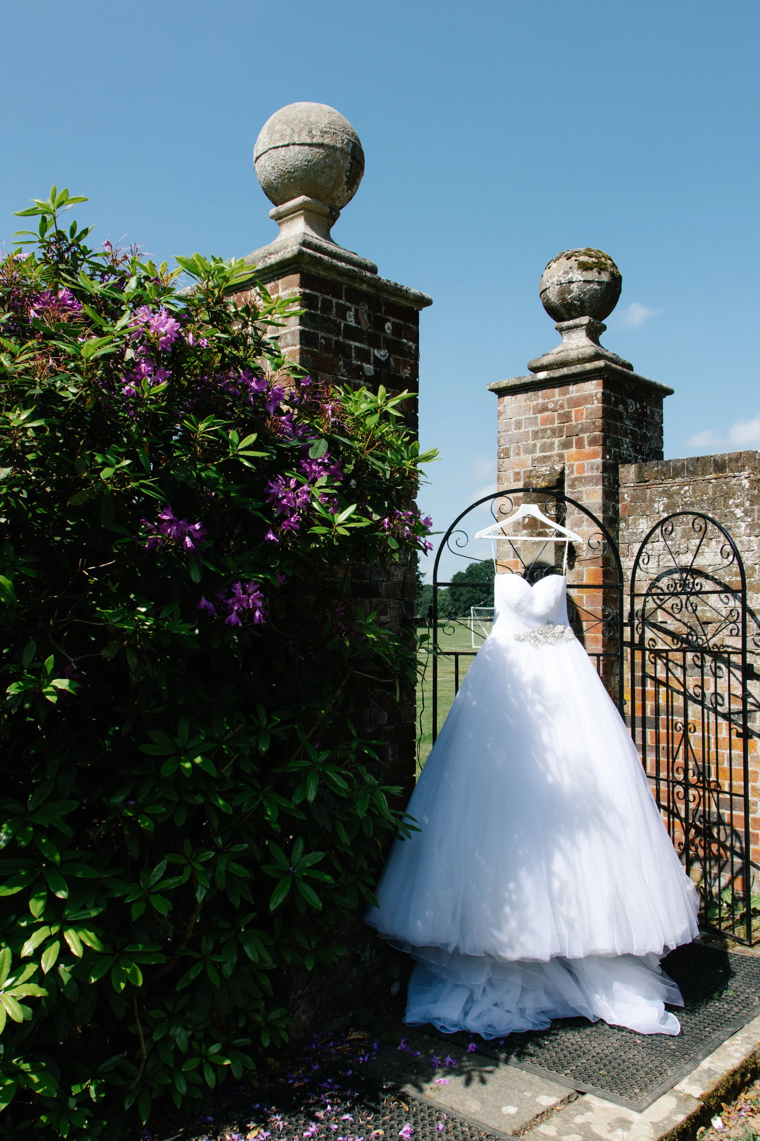 White wedding dress hanging on a brick pillar gate outdoors on a sunny day.