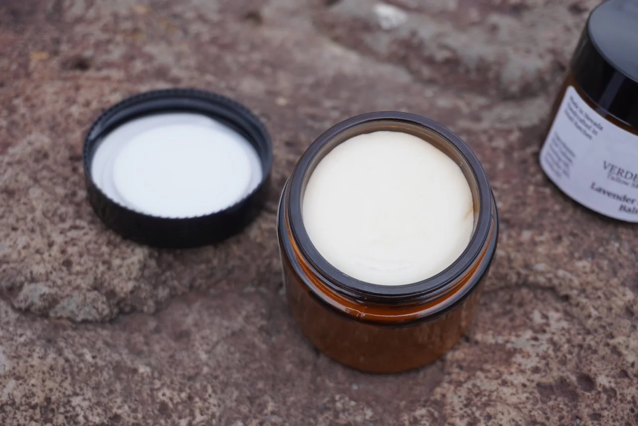 A brown glass jar filled with a creamy white substance, with its black lid removed and placed next to it, on a rocky surface.
