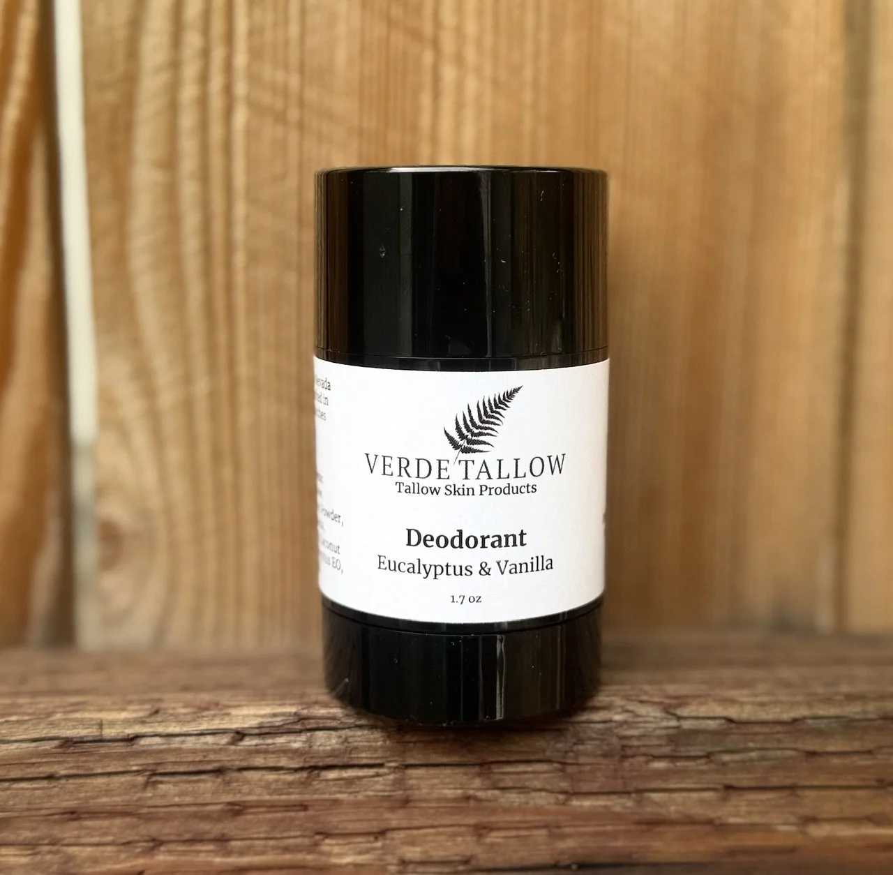 A black container of Verde Tallow deodorant with eucalyptus and vanilla scent, placed on a wooden surface against a wooden background.