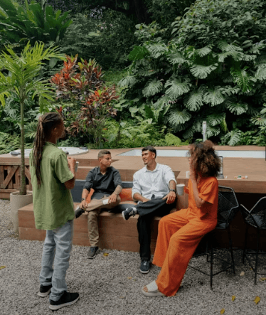 Four people in conversation outdoors surrounded by lush green plants and trees.