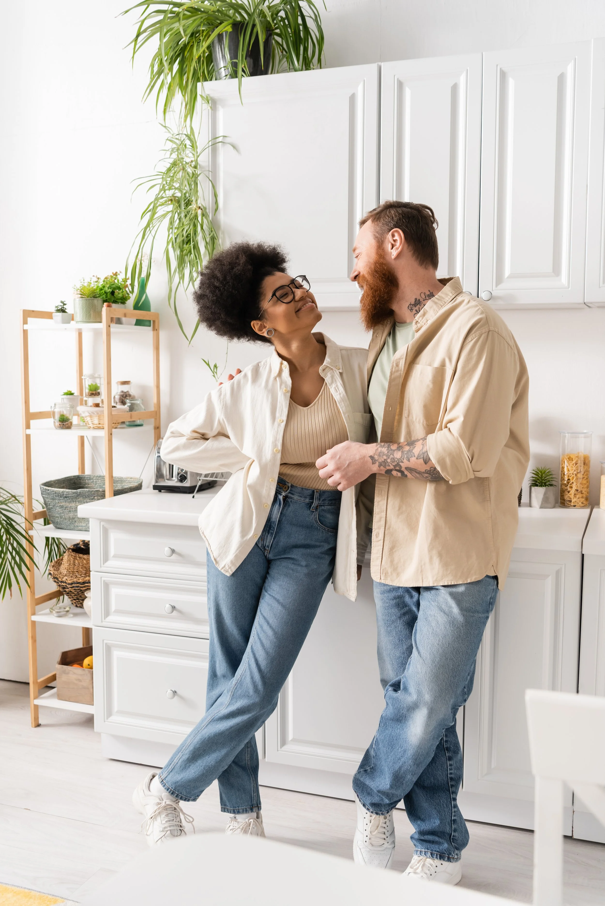 A black woman and a white man smiling at each other in the kitchen lovingly