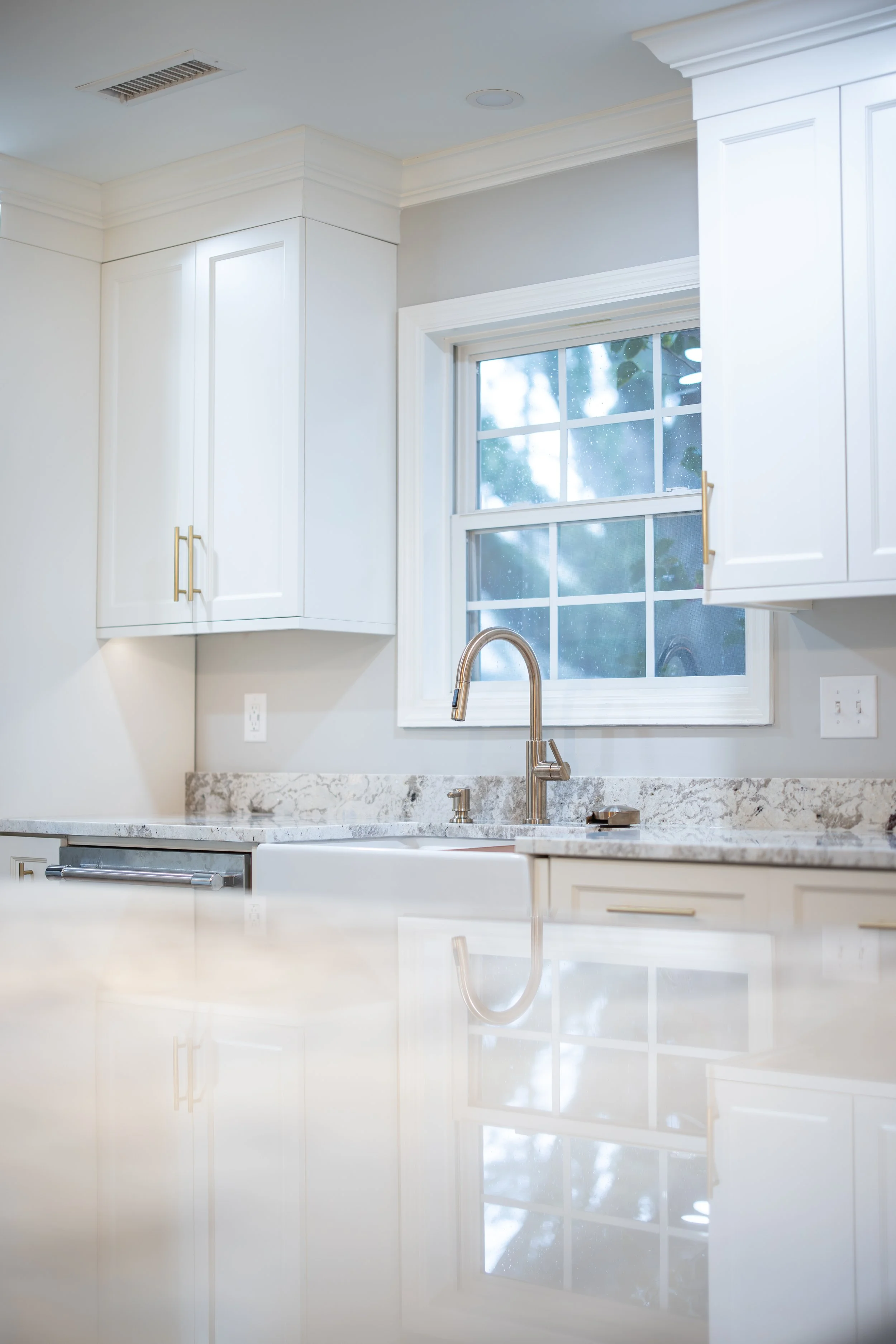 Clean, modern kitchen with white cabinets, marble countertop, stainless steel faucet, and a window with a view outside.